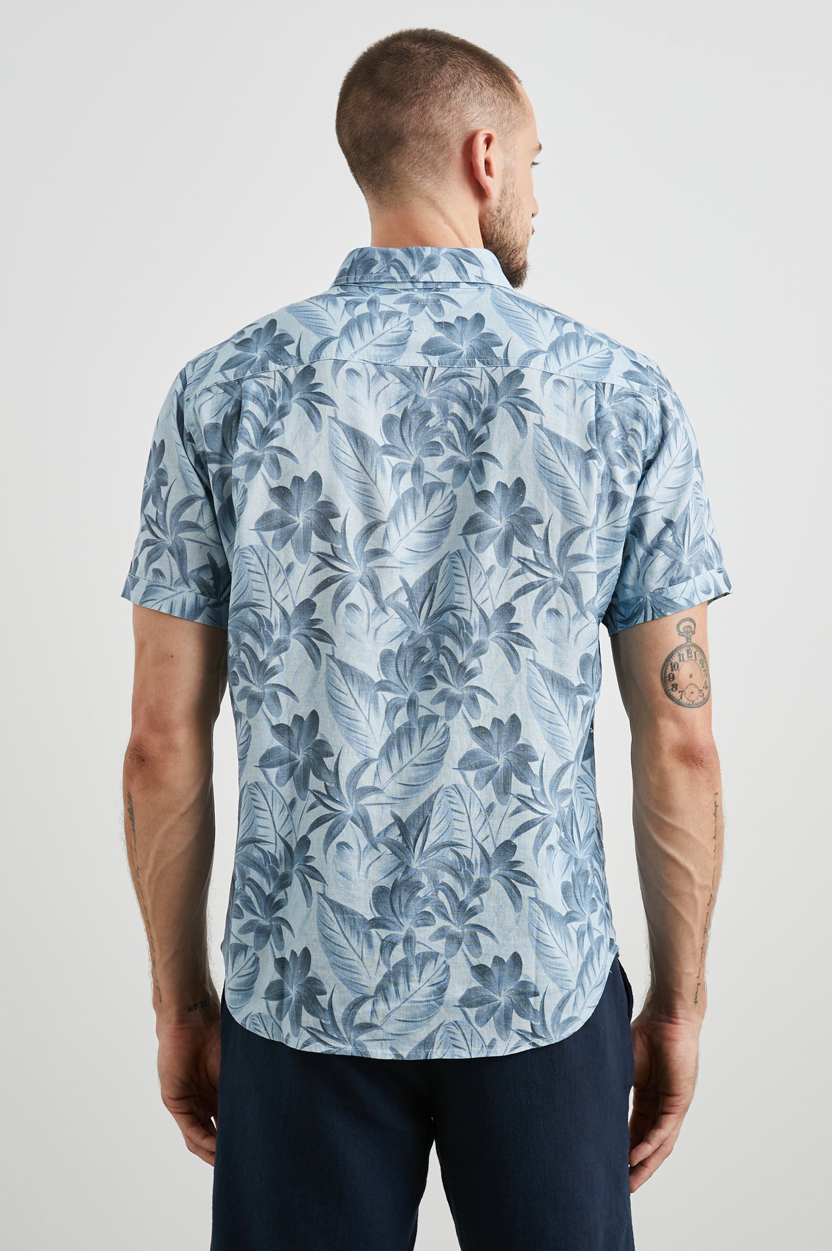 Carson Short Sleeve Button Up with a Chest Patch Pocket in Jungle Garden Reflection Colorway, Flowers and Leaves in Blues on Light Blue - Back View Featured on Model