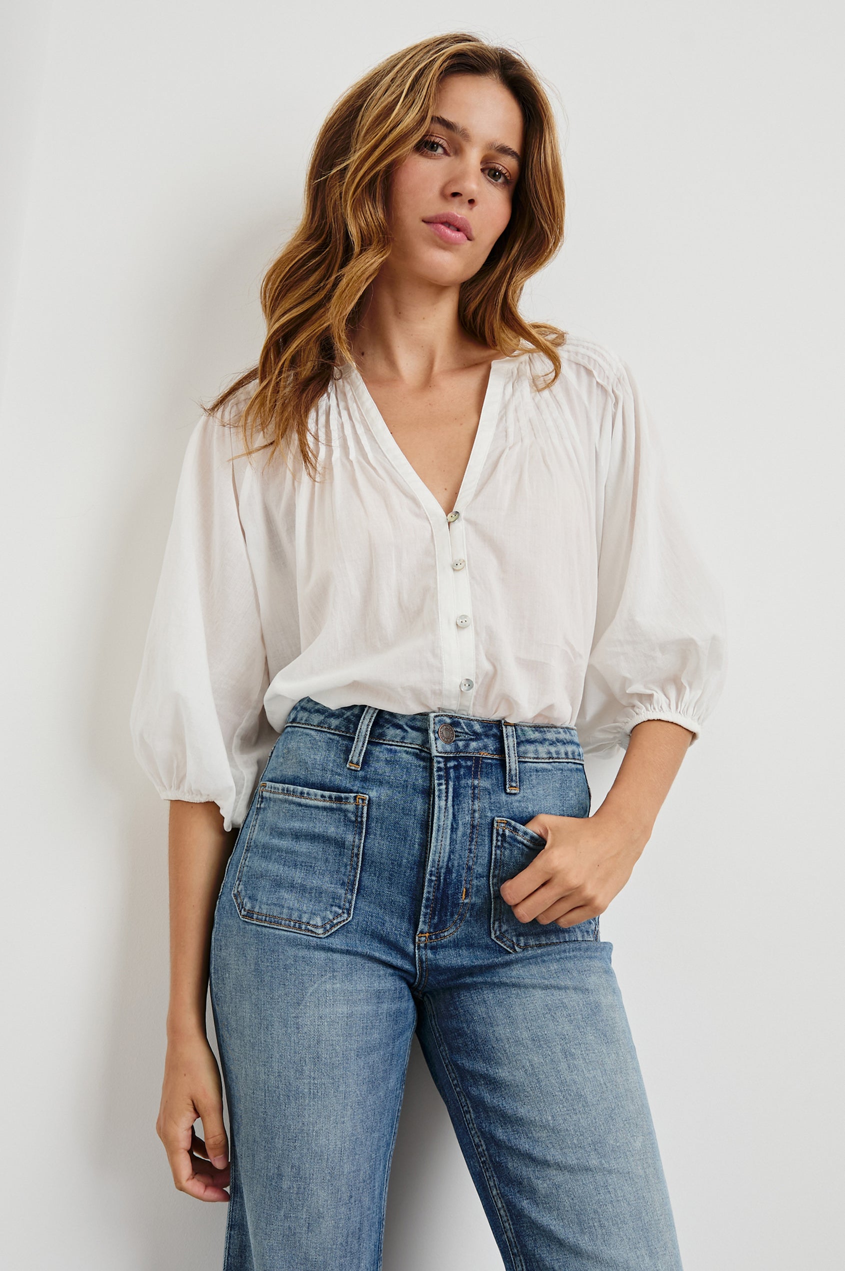 Cassat Blouse with a Deep V-Neckline, Mid-Length Sleeves with Elastic Openings and Pleating around Neckline in White Colorway - Front tucked View Featured on Model
