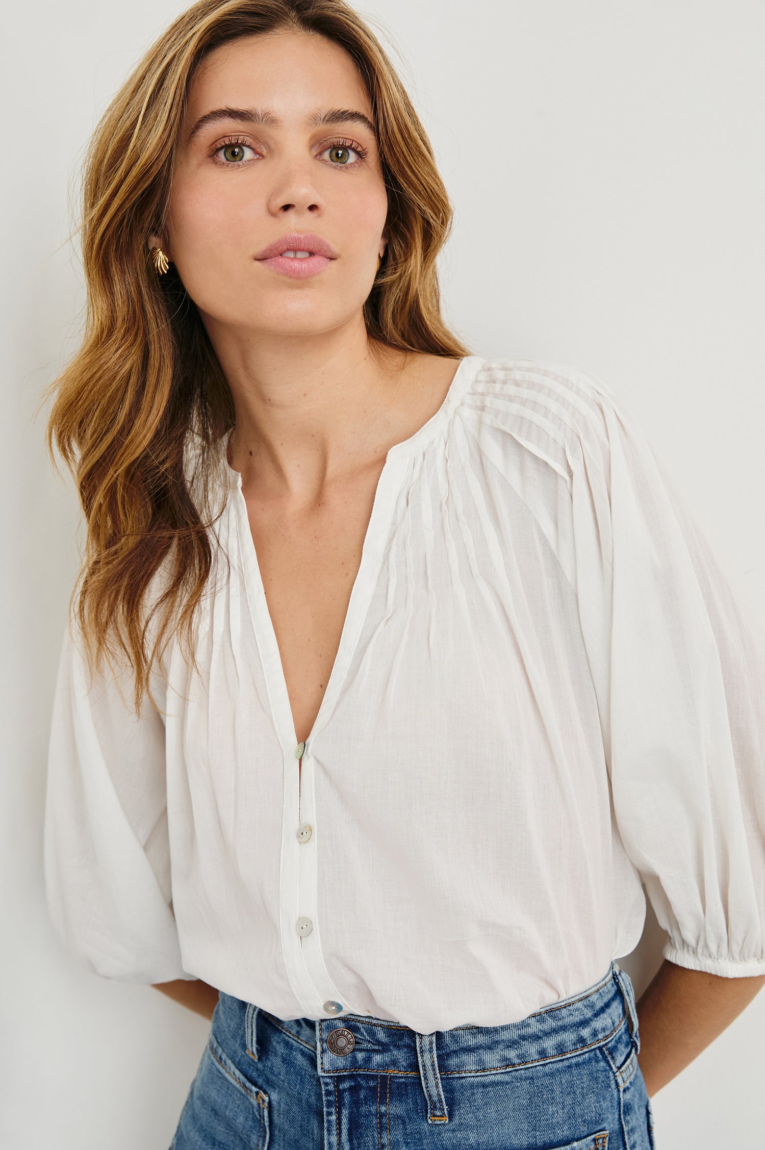 Cassat Blouse with a Deep V-Neckline, Mid-Length Sleeves with Elastic Openings and Pleating around Neckline in White Colorway - Front tucked View Featured on Model