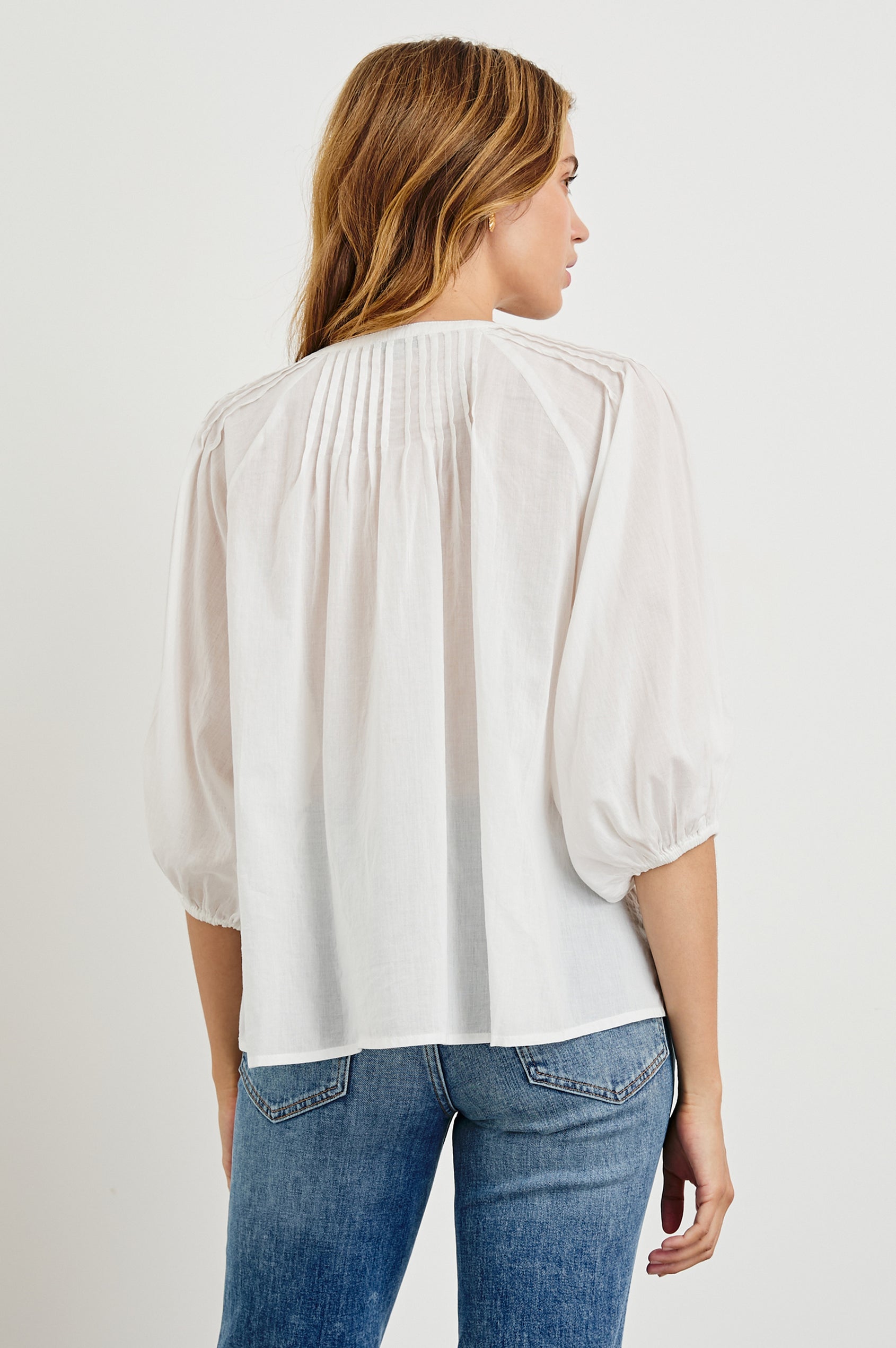 Cassat Blouse with a Deep V-Neckline, Mid-Length Sleeves with Elastic Openings and Pleating around Neckline in White Colorway - Back Untucked View Featured on Model