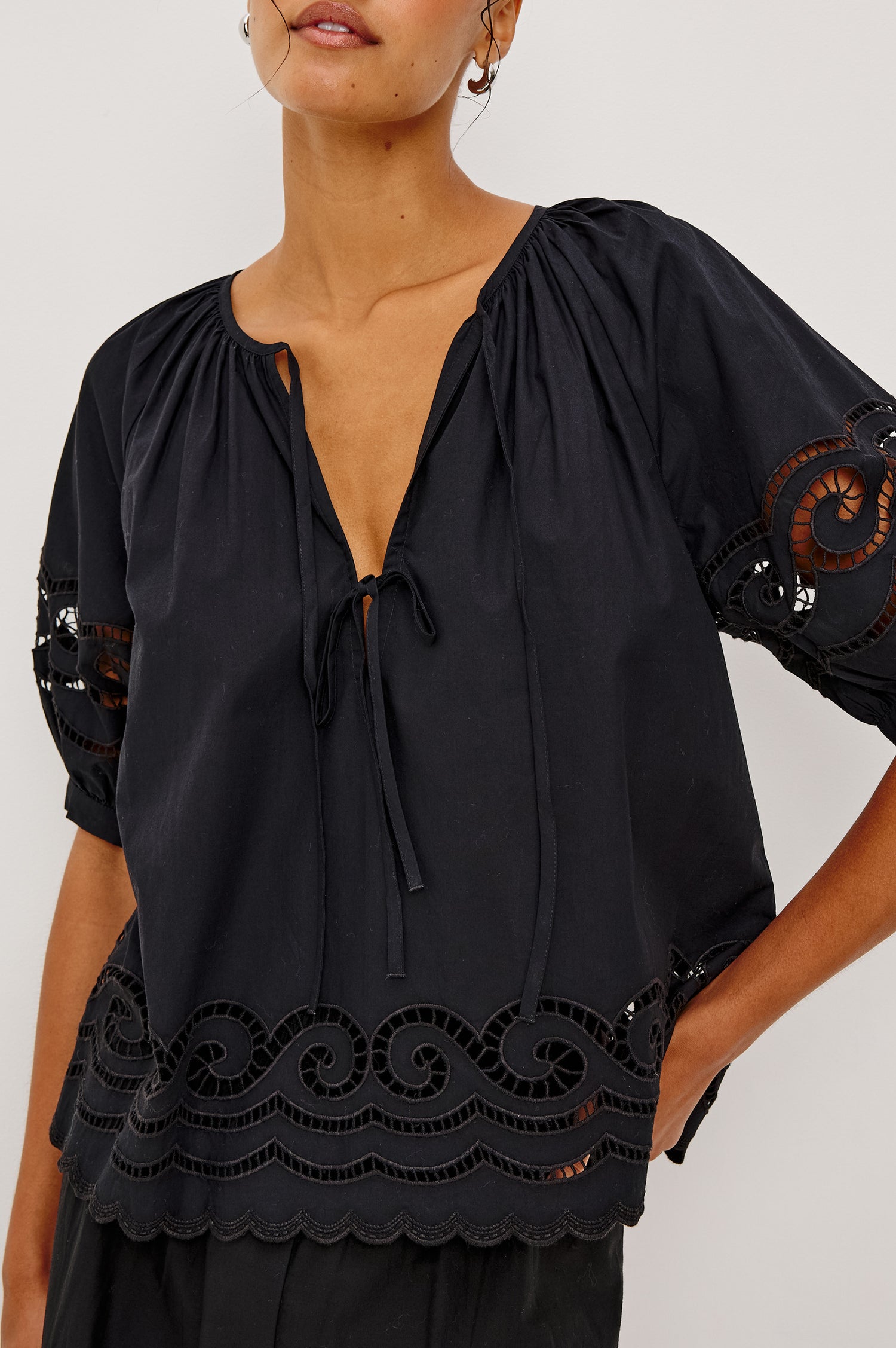 Catalene Peasant Blouse in Poplin With Self-Tie V-Neckline, Sheer Embroidered Detailing, Loose Fit, and Short Puff Sleeves in Black Colorway - Upper Body Close Up Front View Featured on Model