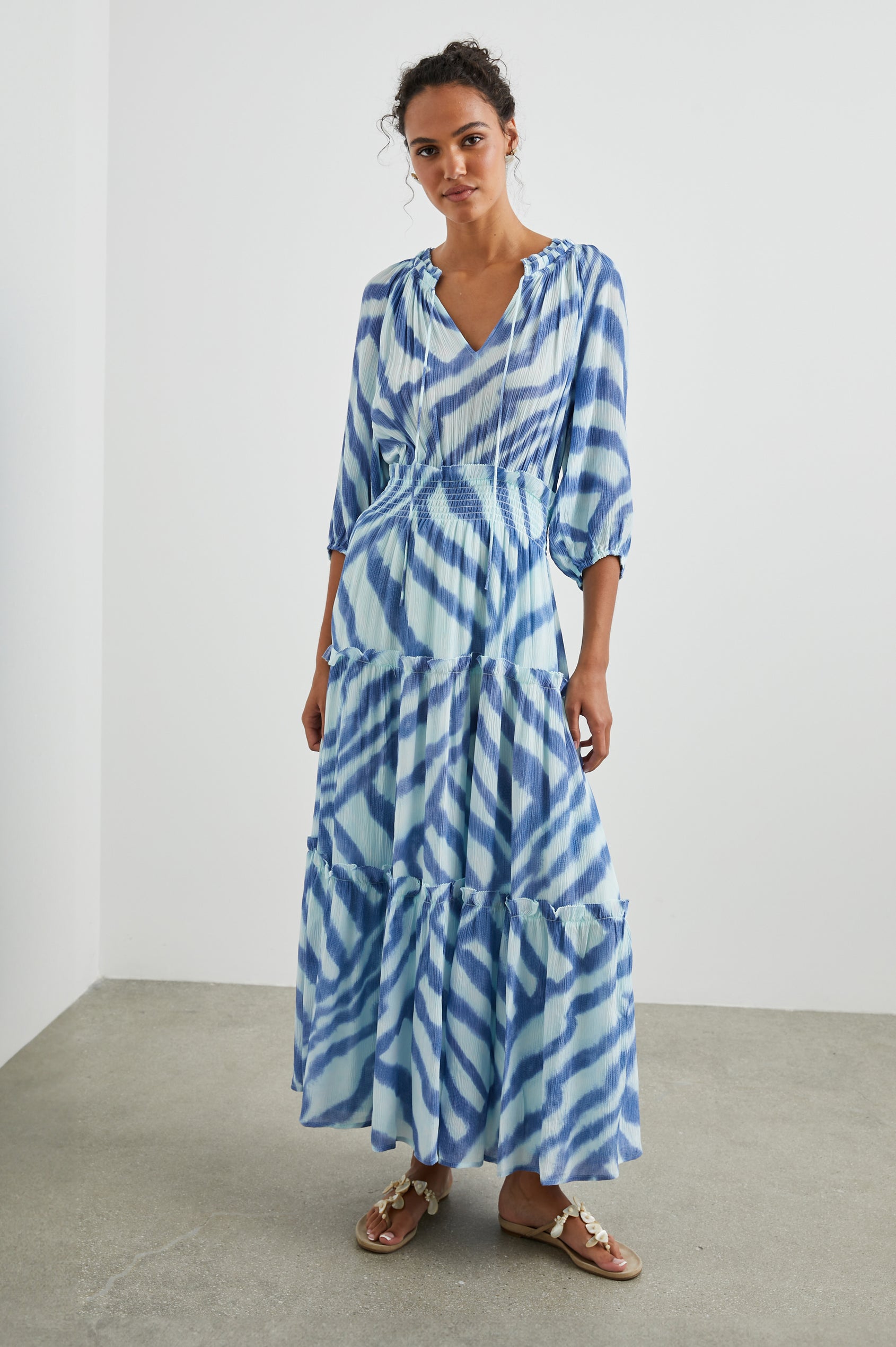 Caterine Maxi Dress with Mid-length Sleeves, a V neck, a Shirred Collar with a tie, a Smocked Waist, and a Tiered Skirt in Blue Watercolor Stripes Colorway, a pattern with blue on light blue - Front Full Body View Featured on Model