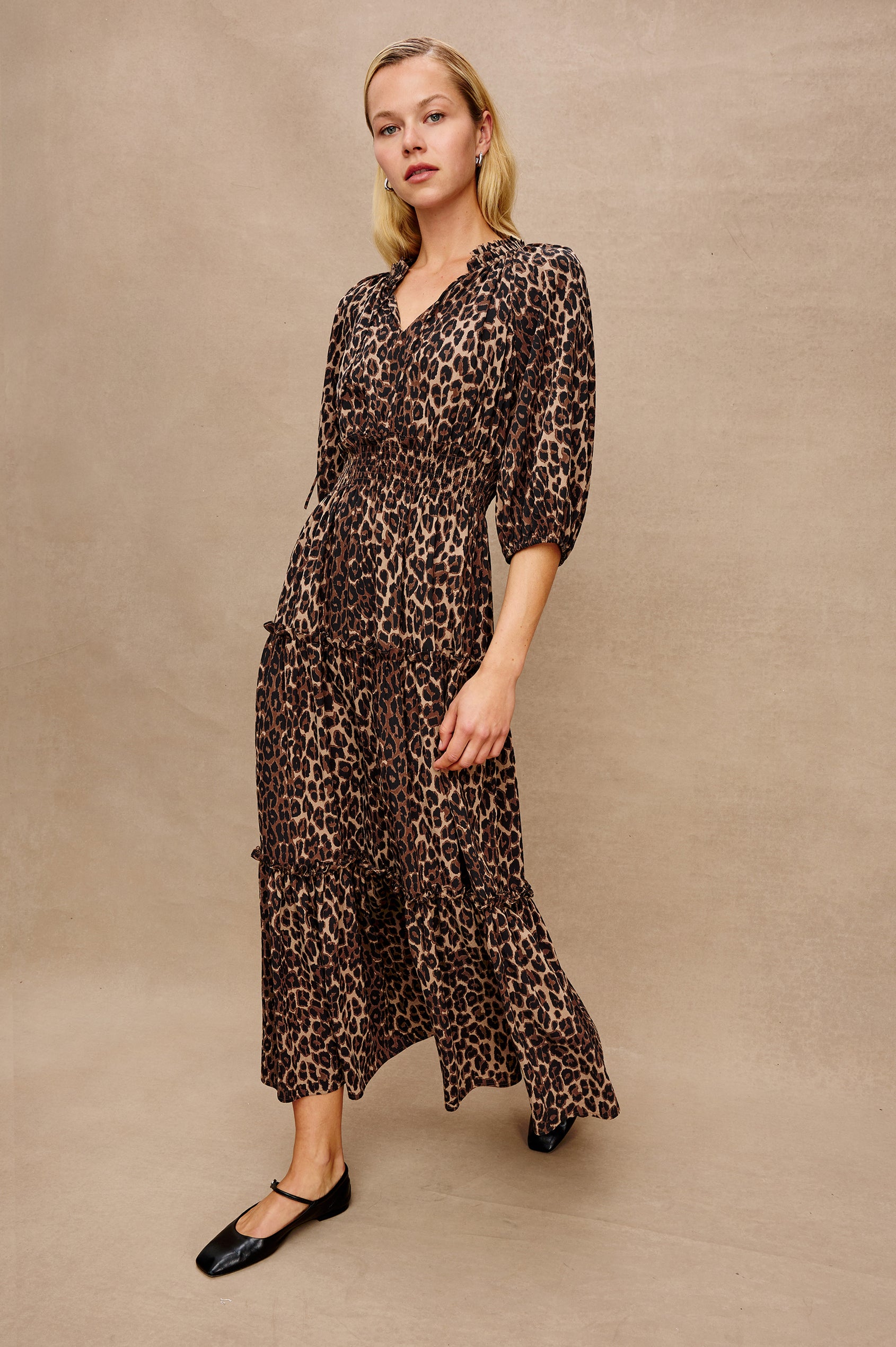 Caterine Maxi Dress with Mid-length Sleeves, a V neck, a Shirred Collar with a tie, a Smocked Waist, and a Tiered Skirt in Brown Nala Colorway - Stylized Front View Featured on Model