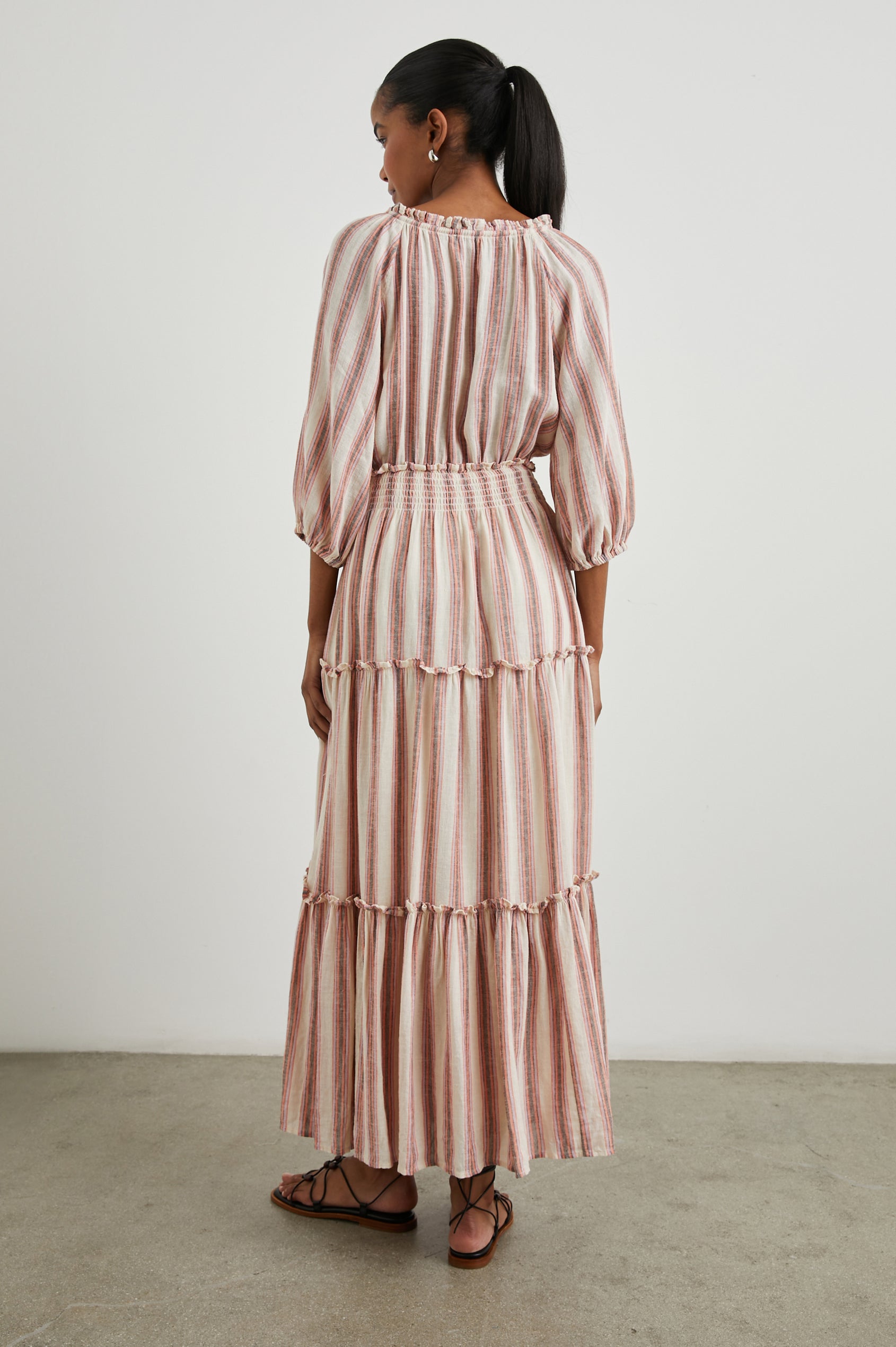 Caterine Maxi Dress with Mid-length Sleeves, a V neck, a Shirred Collar with a tie, a Smocked Waist, and a Tiered Skirt in Camino Stripe Colorway, a vertical stripe with cream, grey, purple and orange  - Back Full Body View Featured on Model