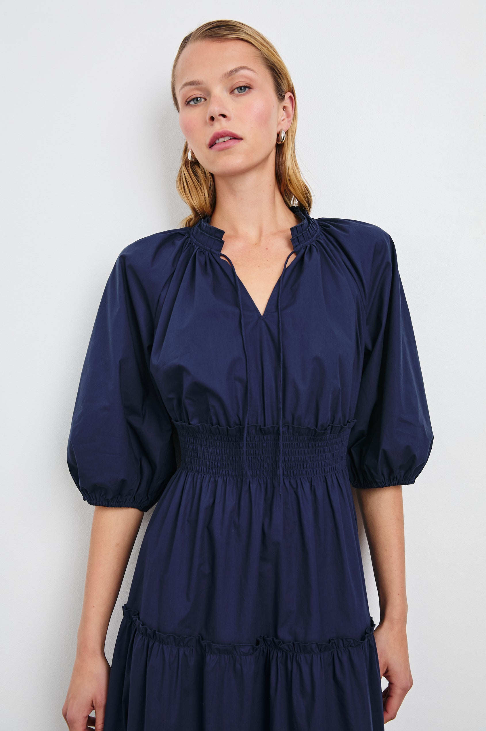 Caterine Maxi Dress with Mid-length Sleeves, a V neck, a Shirred Collar with a tie, a Smocked Waist, and a Tiered Skirt in Navy Colorway - Front View Featured on Model