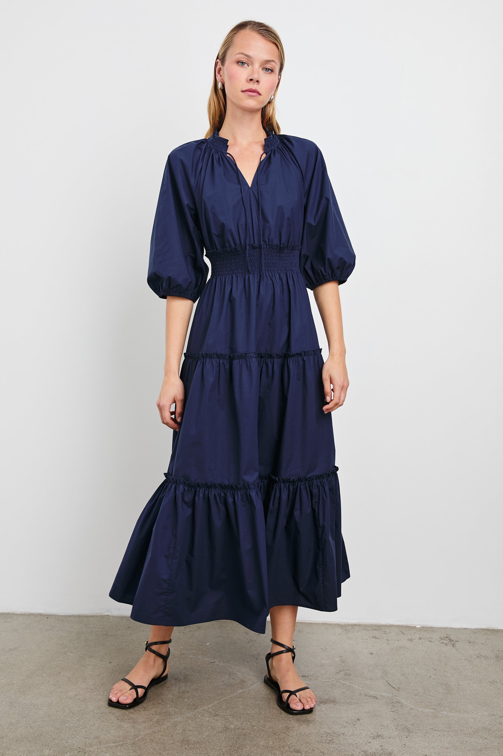 Caterine Maxi Dress with Mid-length Sleeves, a V neck, a Shirred Collar with a tie, a Smocked Waist, and a Tiered Skirt in Navy Colorway - Front Full Body View Featured on Model