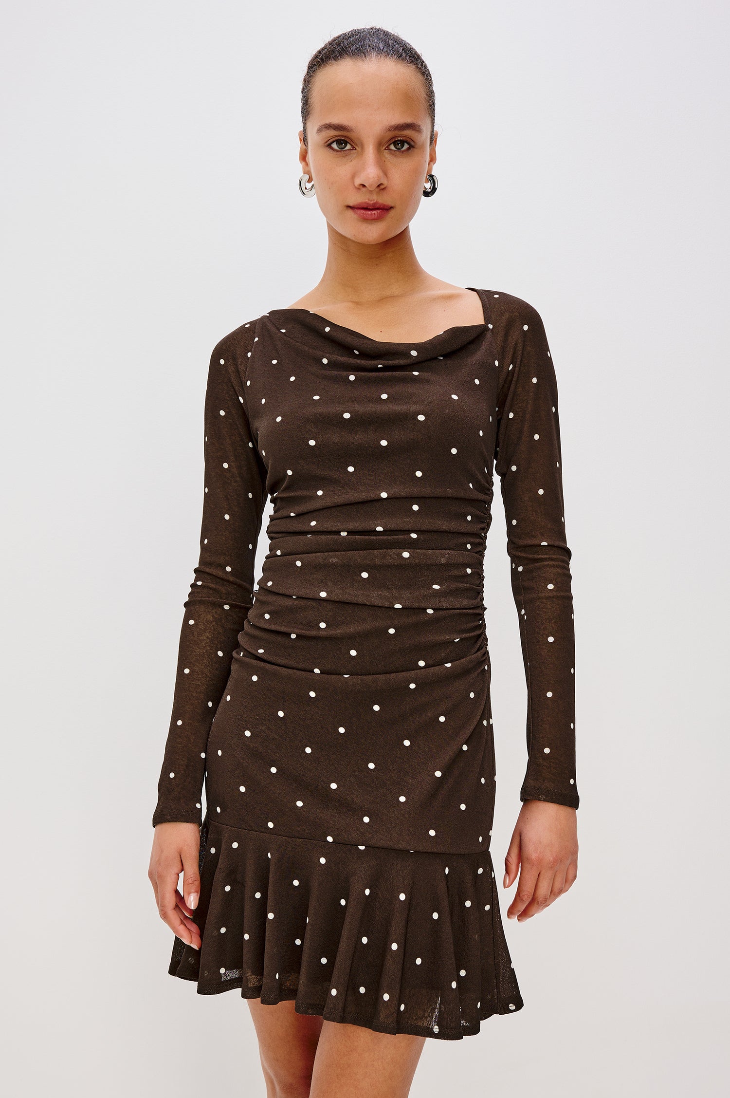 A cocoa-brown mesh midi dress with playful polka dots. The dress has an asymmetrical cowl neckline, long raglan sleeves, shirring at the waist, and a bias-cut skirt. Front View Featured on Model