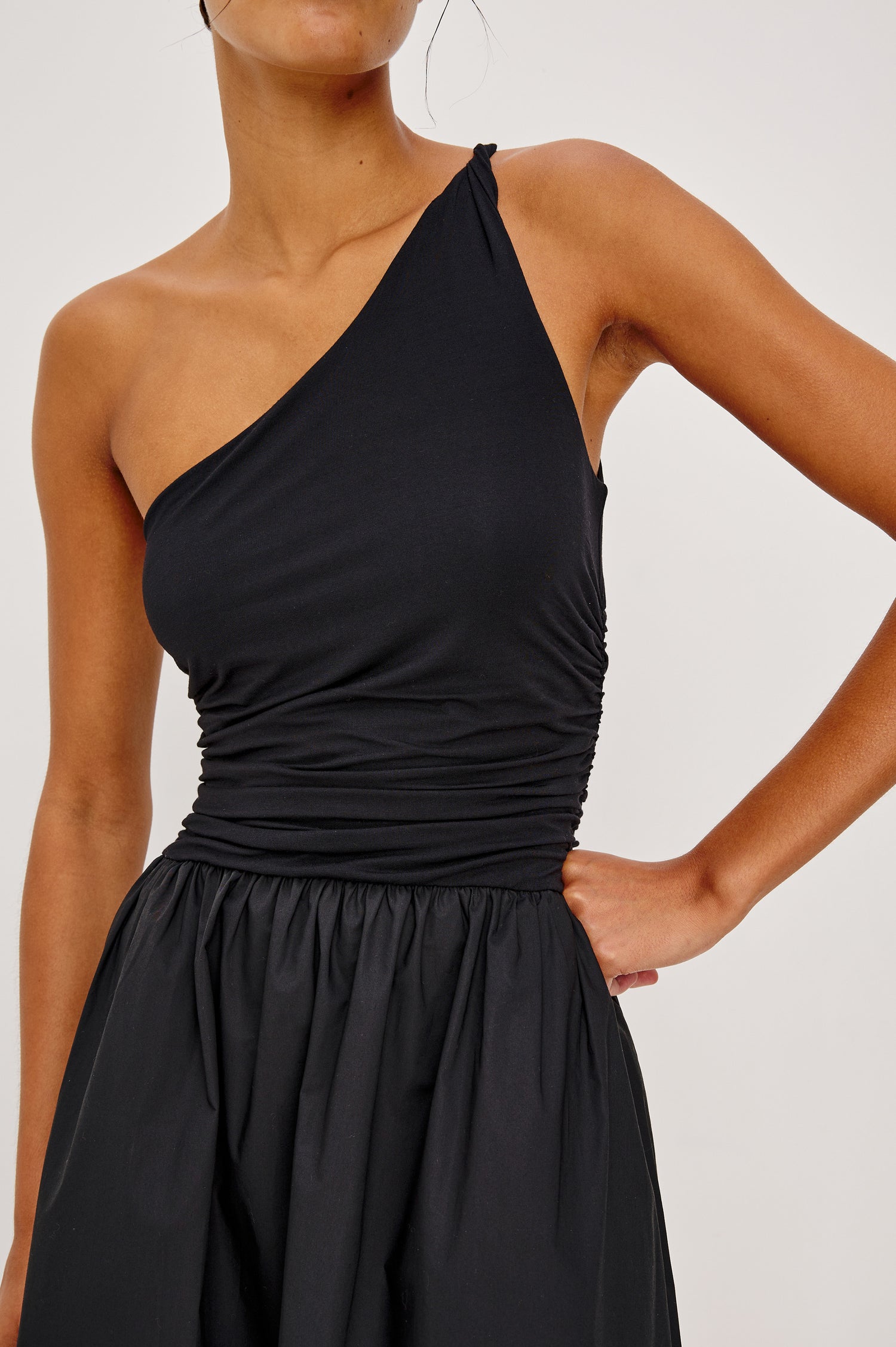 Chayana Midi Dress in Jersey With One-Shoulder Twist Strap Neckline, Waist Shirring, Side Pockets, Poplin Skirt in Black Colorway - Upper Body Close Up View Featured on Model