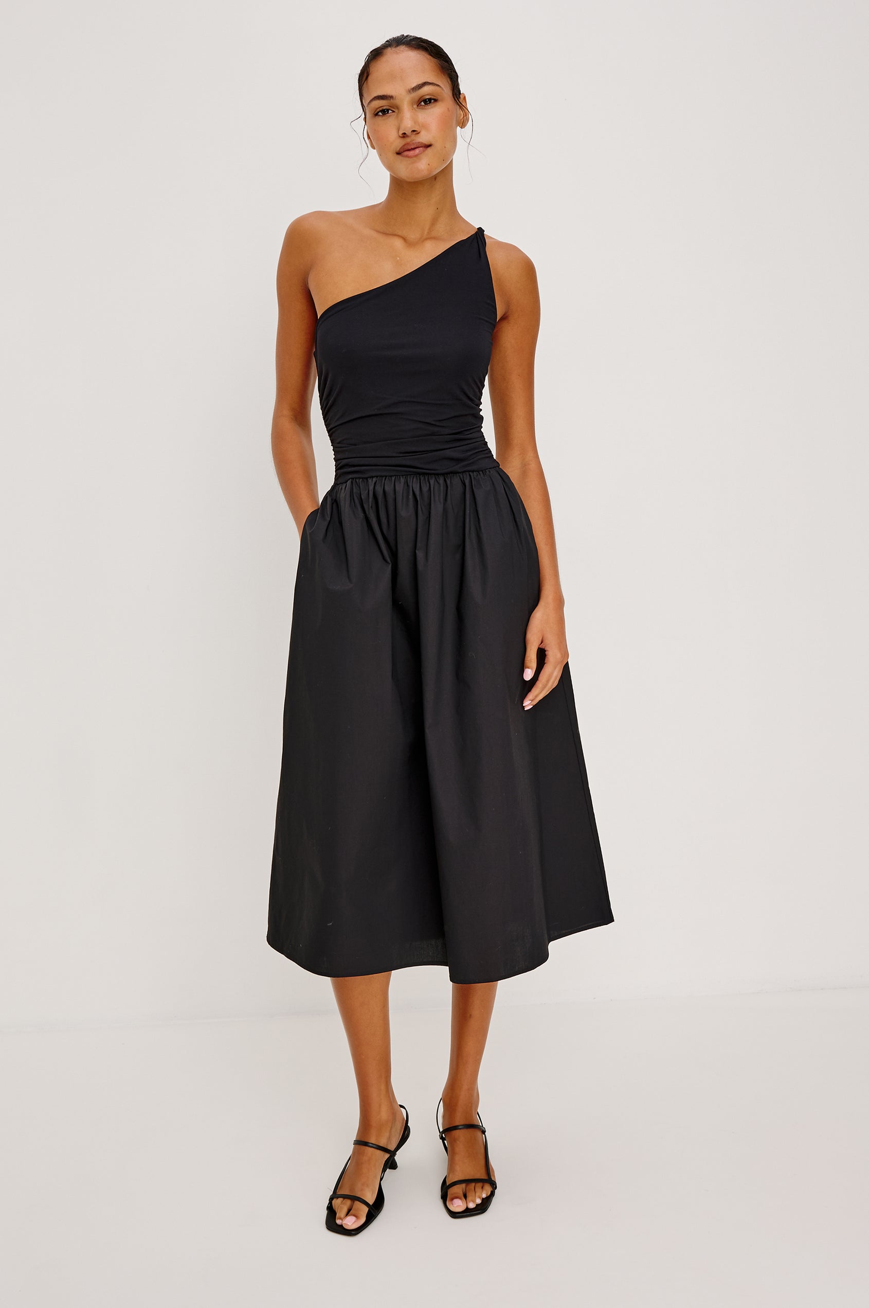Chayana Midi Dress in Jersey With One-Shoulder Twist Strap Neckline, Waist Shirring, Side Pockets, Poplin Skirt in Black Colorway - Full Body Front View Featured on Model