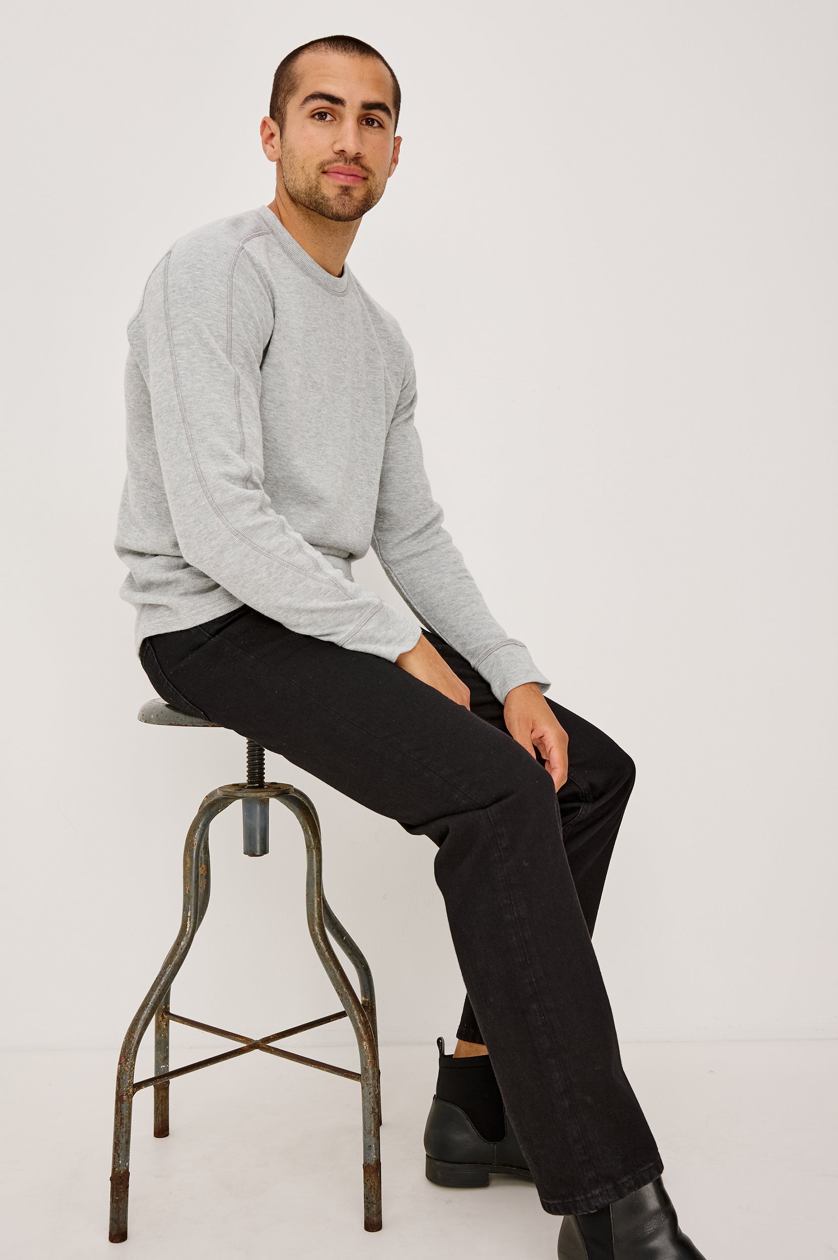 Clayton Slim Straight Jean With 5-Pocket Styling, Belt Loops, and Front Zip-Fly in Dark Black Colorway - Full Body Front View Featured on Model Sitting