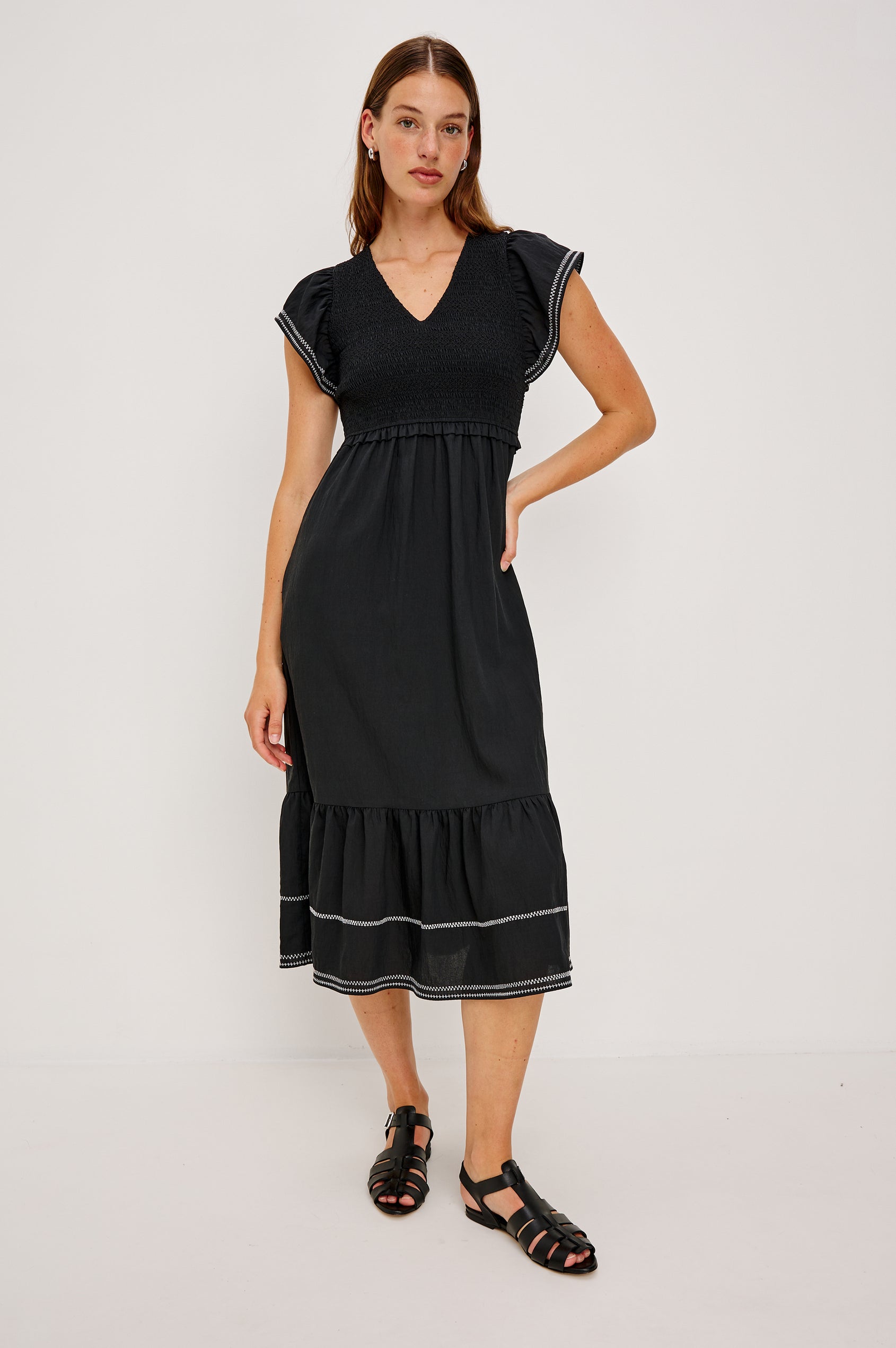 Clementine Midi Dress with a Deep V Neckline, Flutter Sleeves, Smocked Top, Two Side Pockets and contrast white stitching on the Sleeves and Hem in Black Colorway- Front Full Body View Featured on Model.
