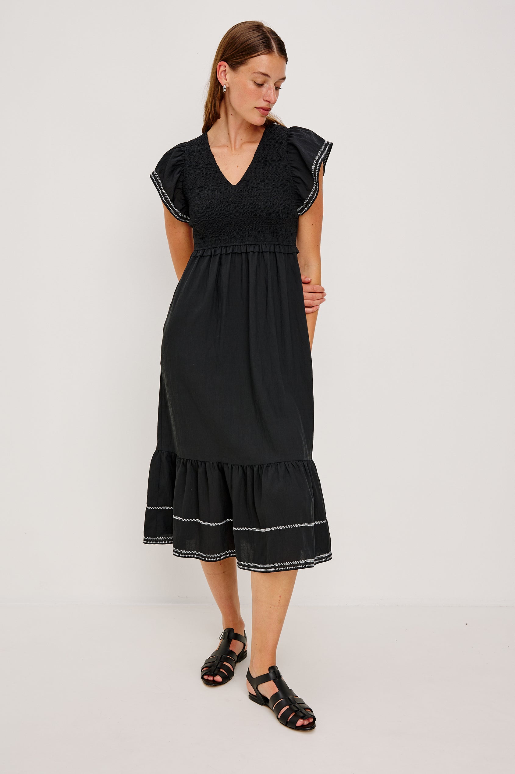 Clementine Midi Dress with a Deep V Neckline, Flutter Sleeves, Smocked Top, Two Side Pockets and contrast white stitching on the Sleeves and Hem in Black Colorway- Front Full Body View Featured on Model.