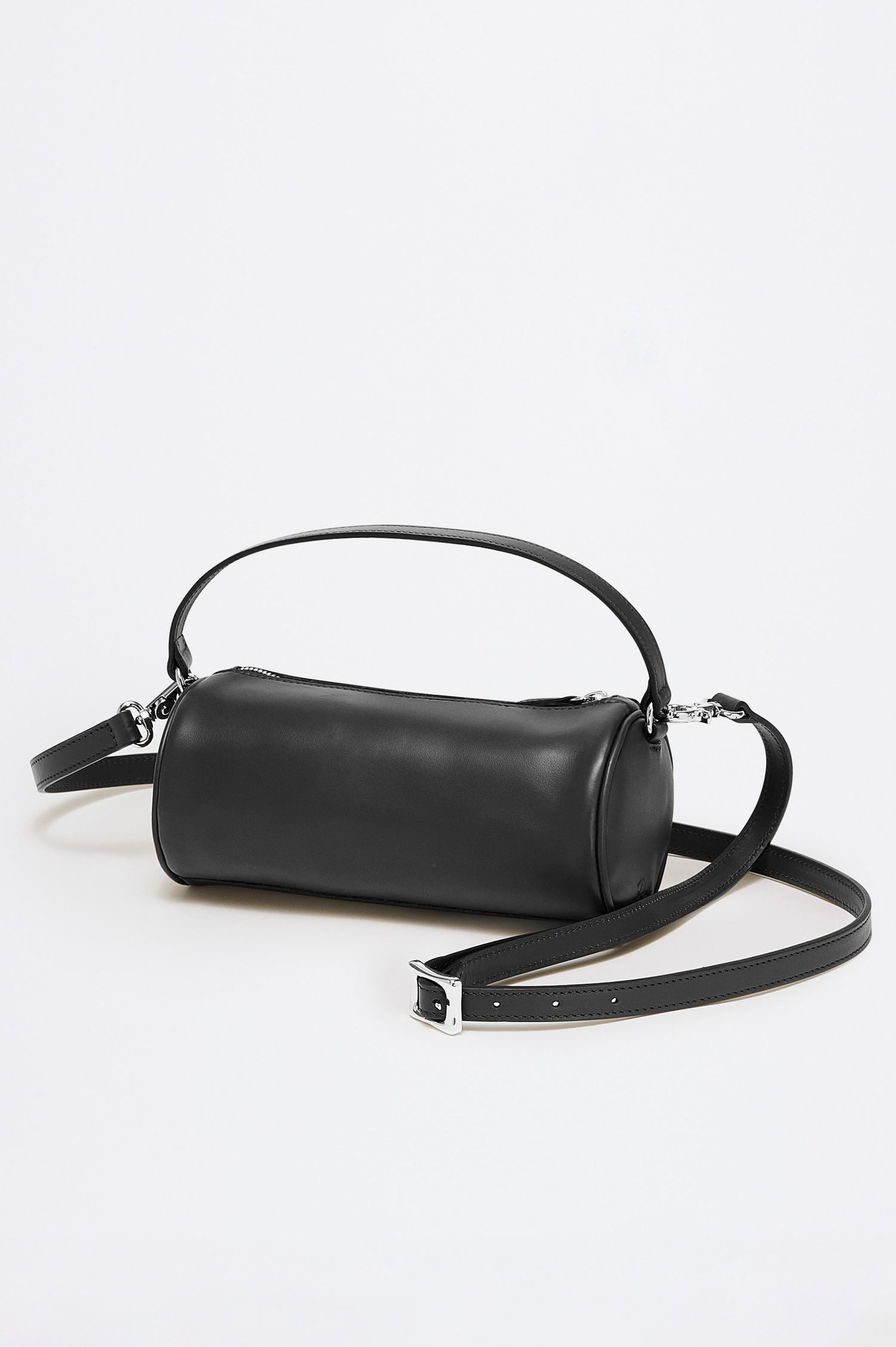 The Como is a mini barrel bag, made from smooth leather with a fixed top strap, a removable and adjustable buckled crossbody strap, a top zip, a side-embossed logo, and a branded interior label, in Black Leather colorway. Front view featured.