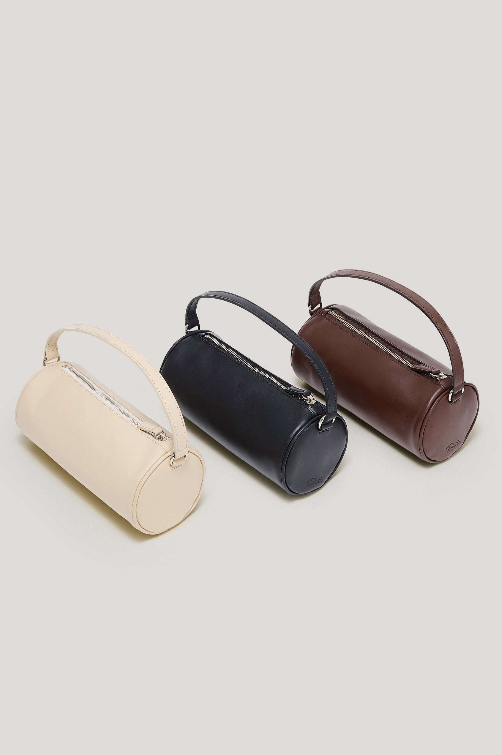 The Como is a mini barrel bag, made from smooth leather with a fixed top strap, a removable and adjustable buckled crossbody strap, a top zip, a side-embossed logo, and a branded interior label, all colorways. Top view of  handbags featured.