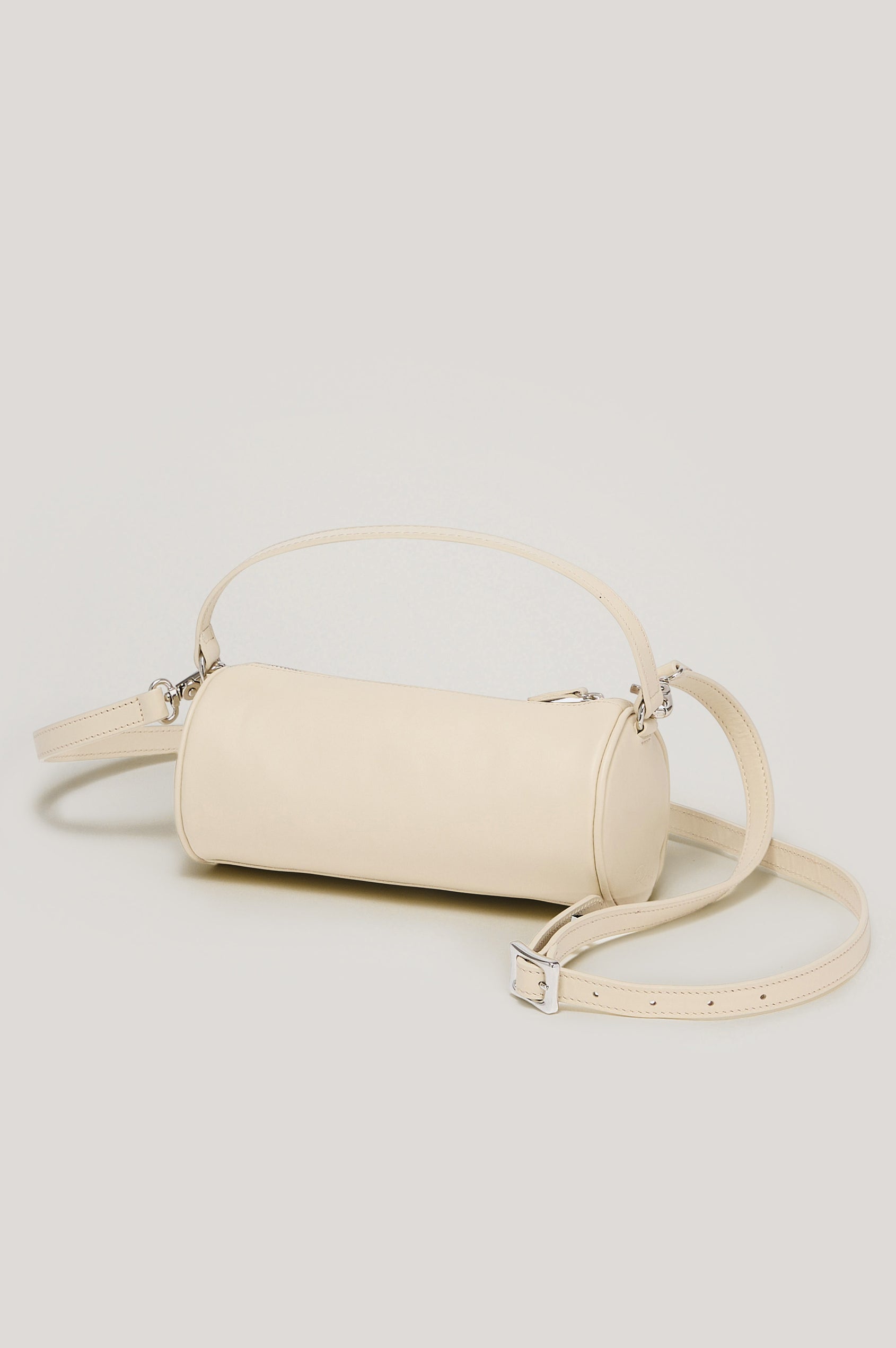 The Como is a mini barrel bag, made from smooth leather with a fixed top strap, a removable and adjustable buckled crossbody strap, a top zip, a side-embossed logo, and a branded interior label, in Bone Leather colorway. Front view featured.