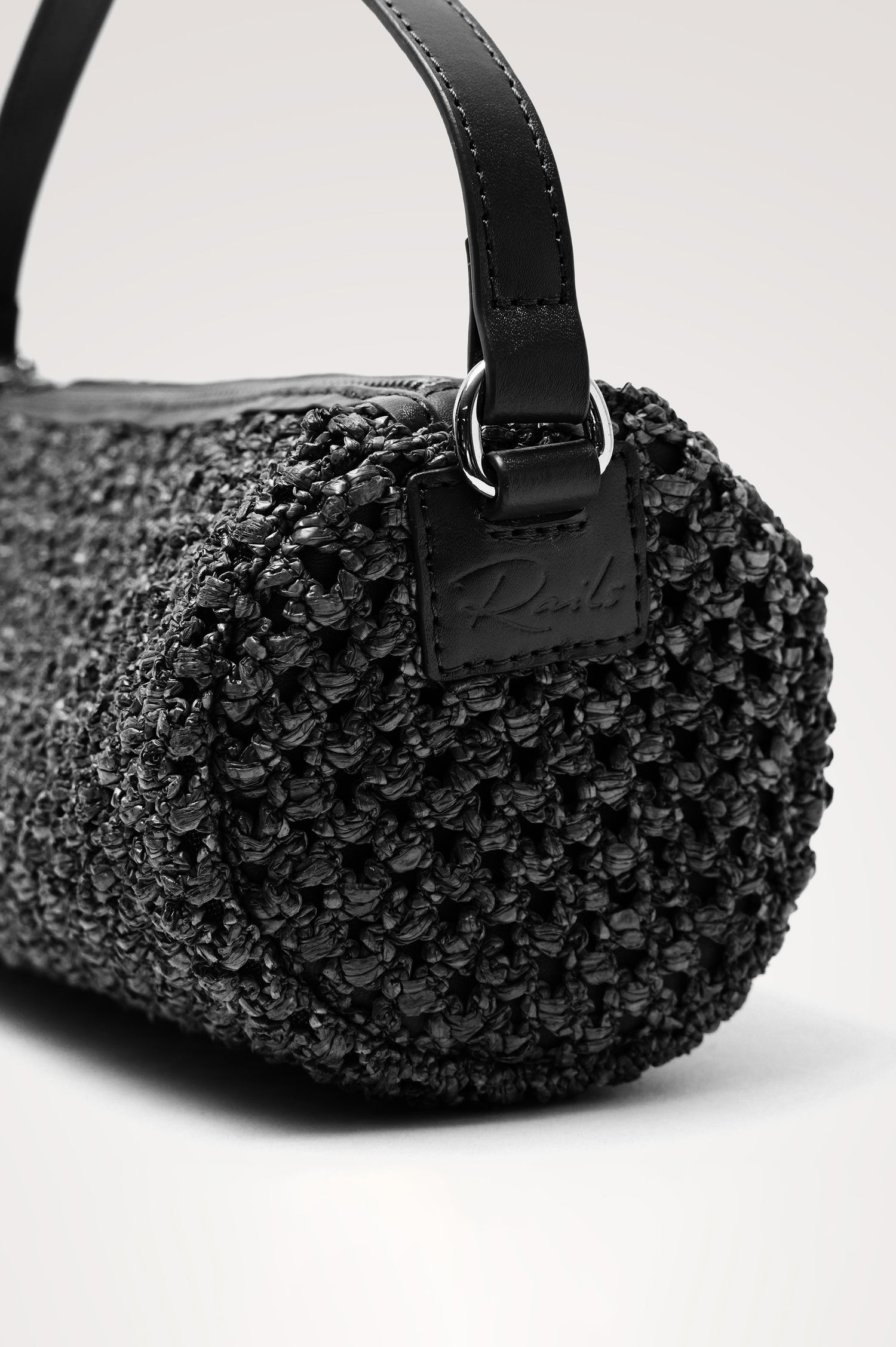 Como Mini Barrel Bag in Woven Raffia With Top Strap, Removable and Adjustable Crossbody Strap, and Top Zip in Black Raffia Colorway - Side Close Up View Featured