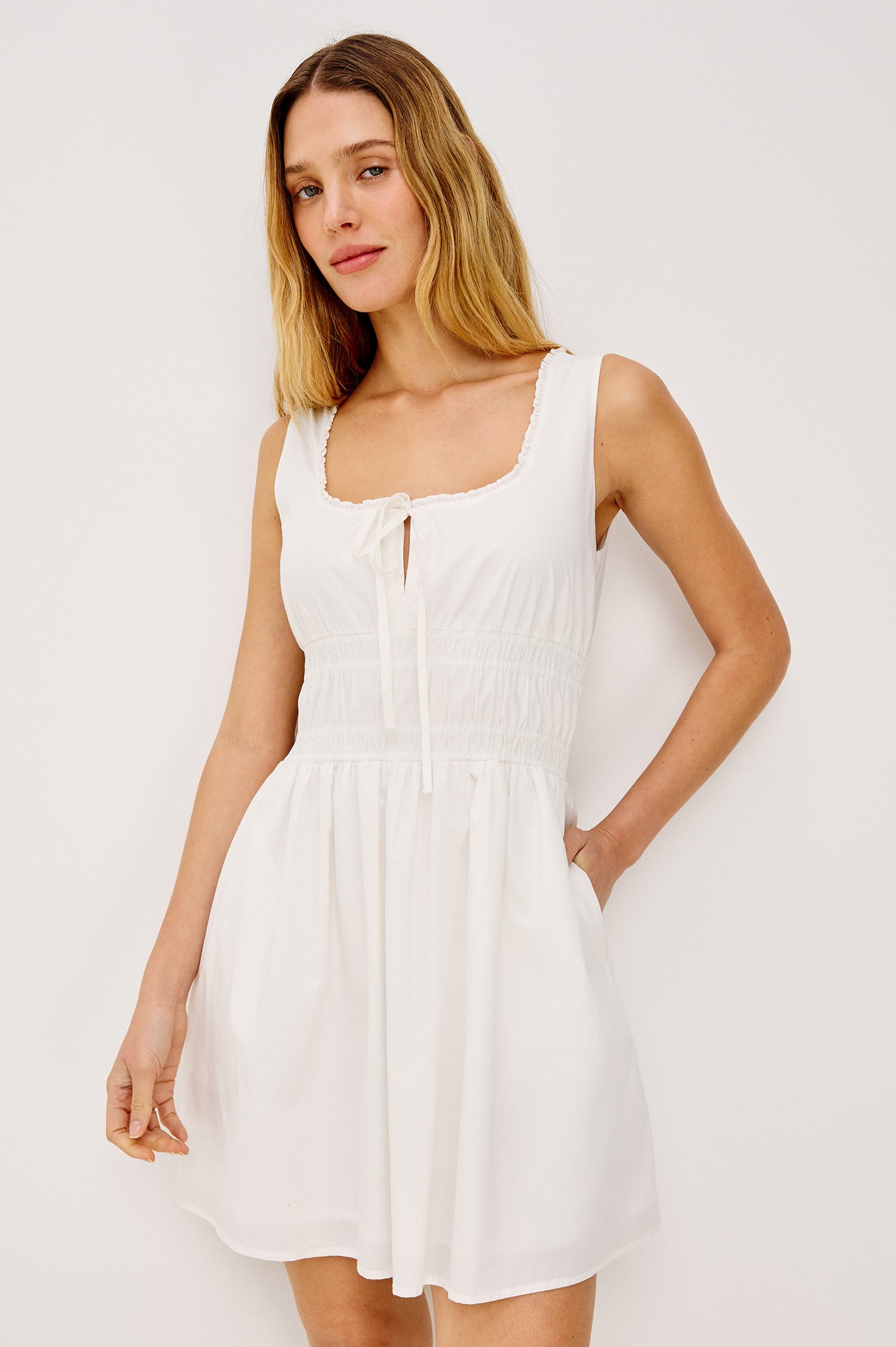 Cosette Mini Dress in Cotton Poplin With Soft Square Neckline, Center-Front Bust Ties, Smocked Waist, Side Pockets, and A-Line Skirt in White Colorway - Upper Body Front View Featured on Model