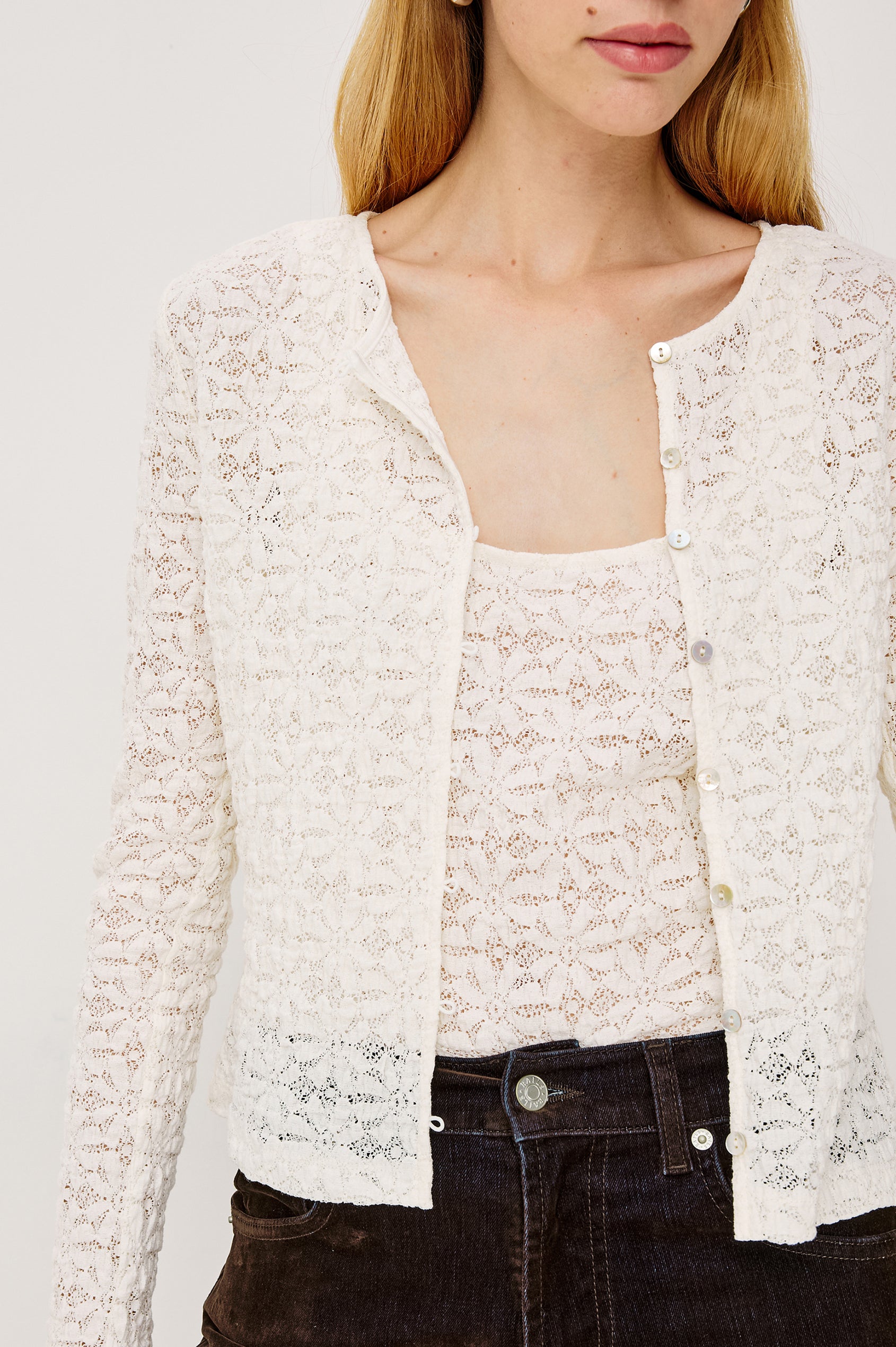 Cyrah is a long sleeve button front lace cardigan in Ivory colorway. Front detailed view of model featured.