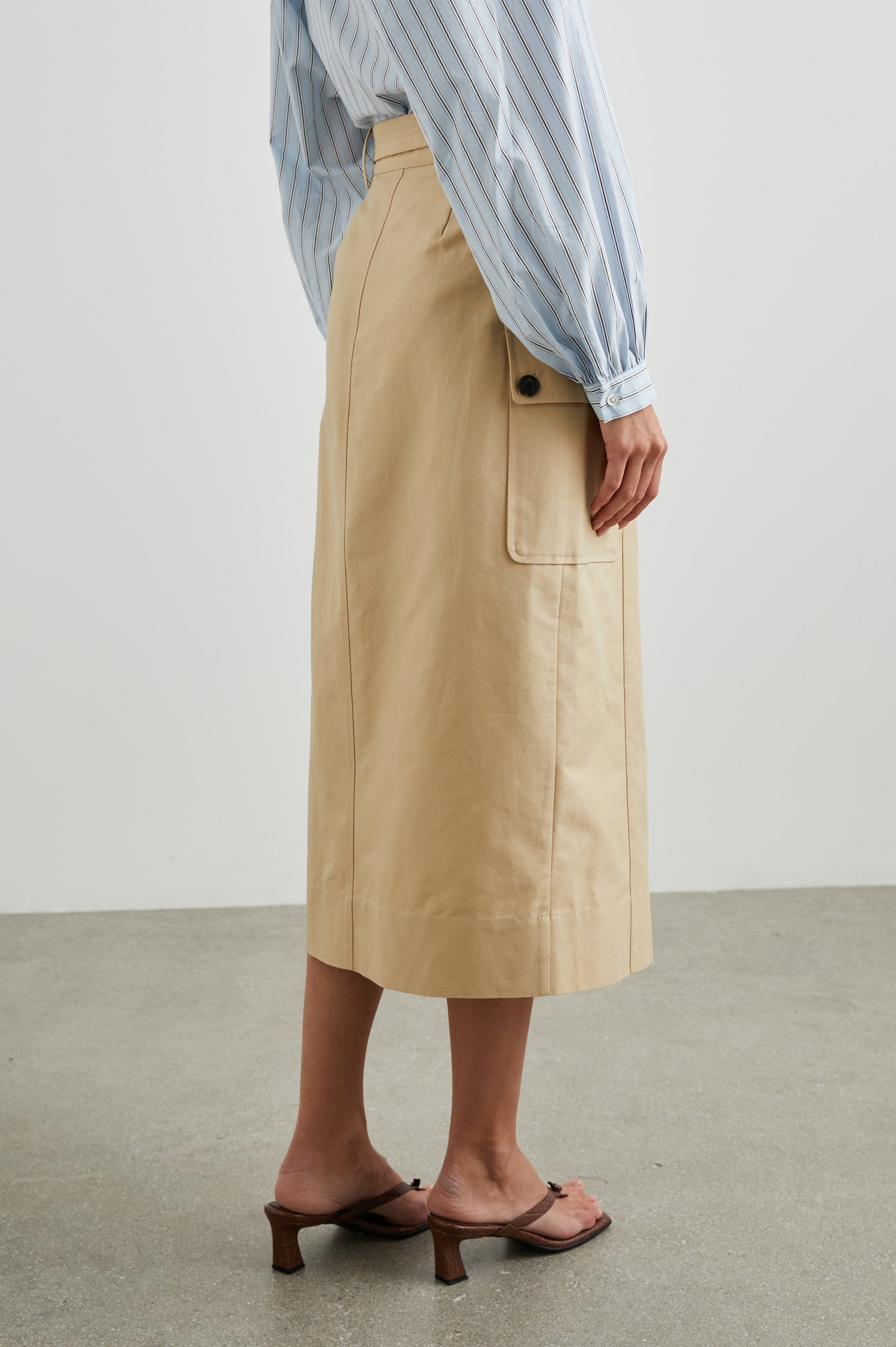 Cyrus Midi Skirt with a Center Slit, Belt Loops, a Fabric Belt, Two Front Pockets and Two Side Button Flap Pockets in Khaki Colorway, with Dark Buttons - Back View Featured on Model 