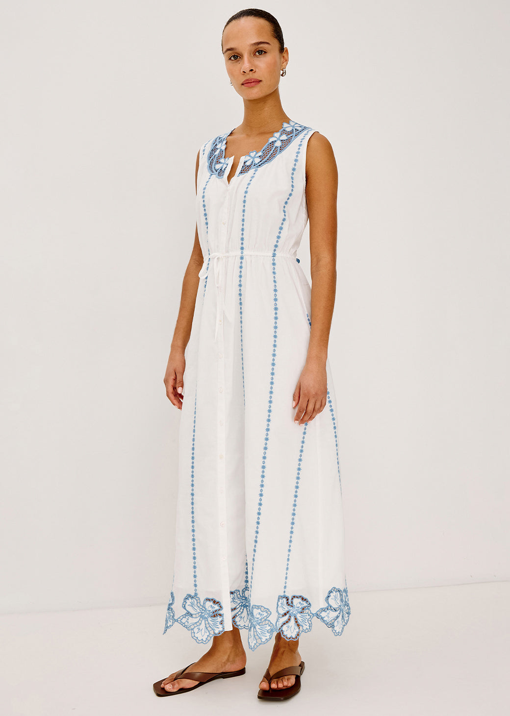 Woman wearing a white dress with blue embroidery on a plain background