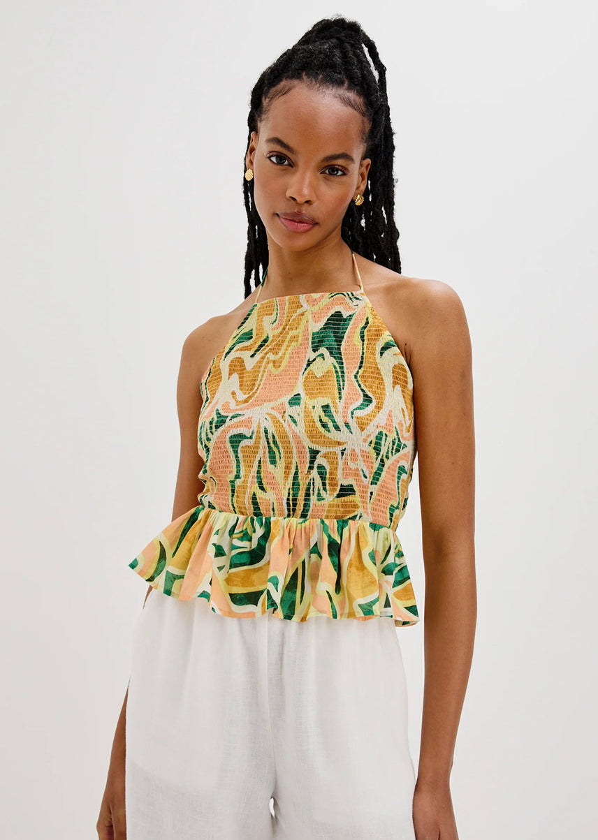 Woman wearing a tropical print top and white pants on a plain background