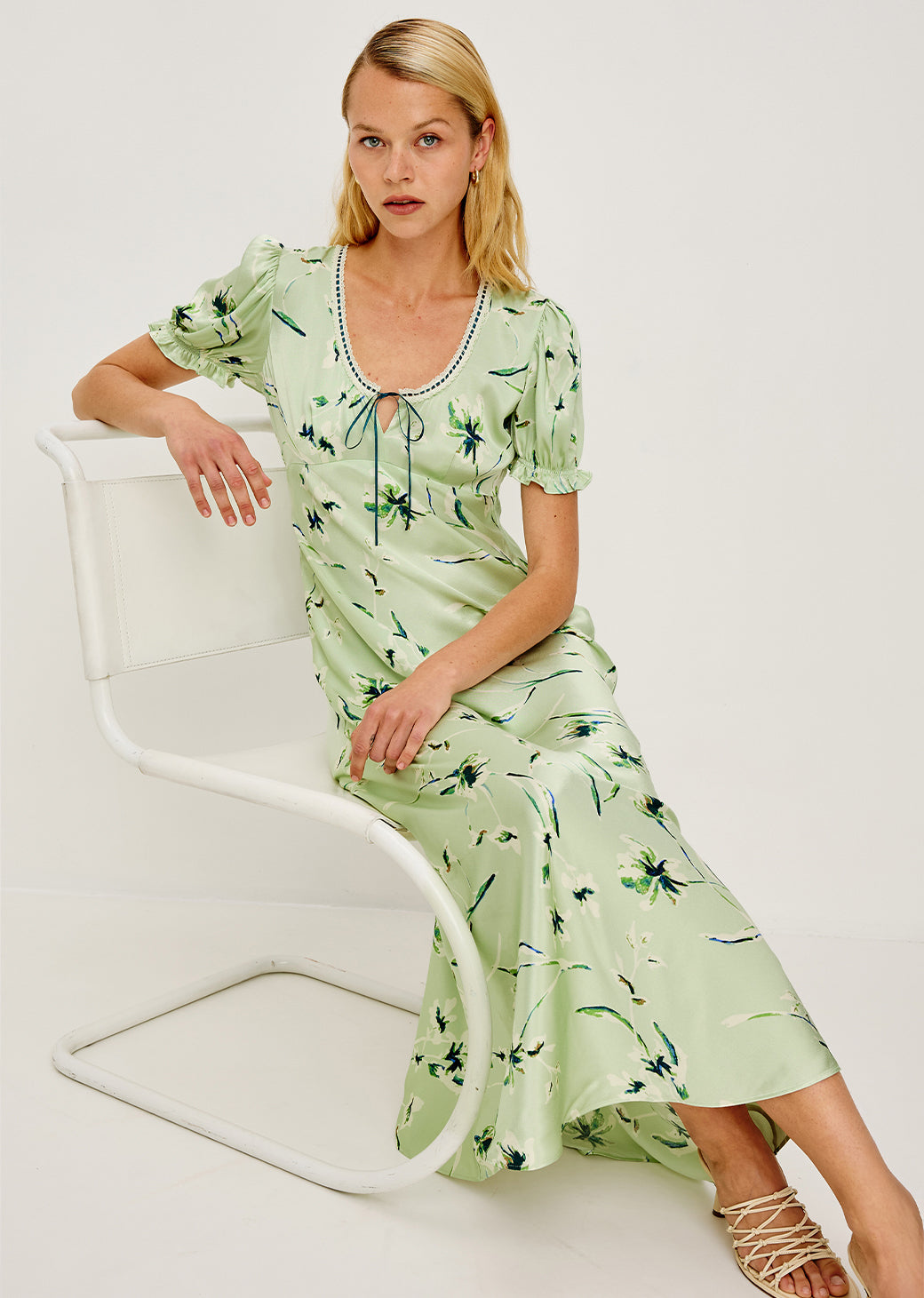 Woman wearing a light green dress with floral pattern sitting on a white chair.