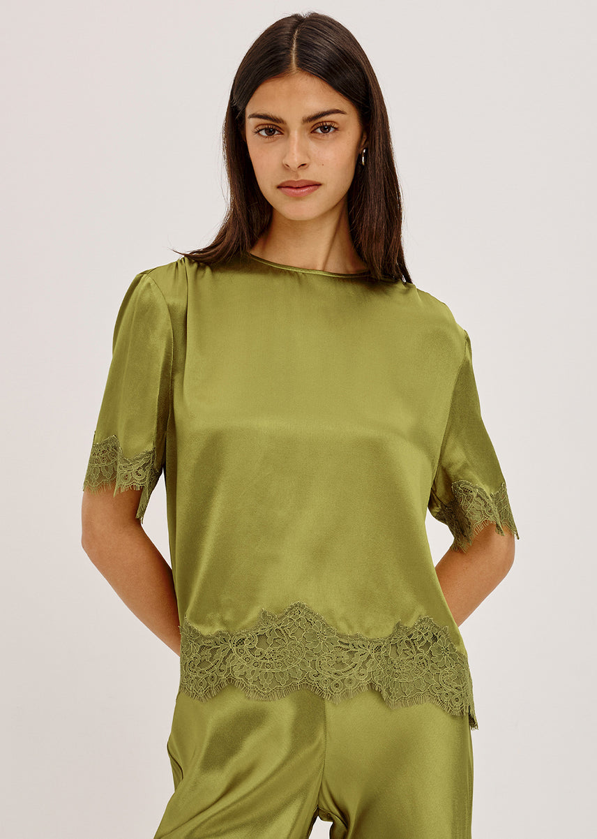 A woman modeling a sage green satin short-sleeve top with matching lace trim at the cuffs and hem, paired with matching satin pants, against a light gray studio background.