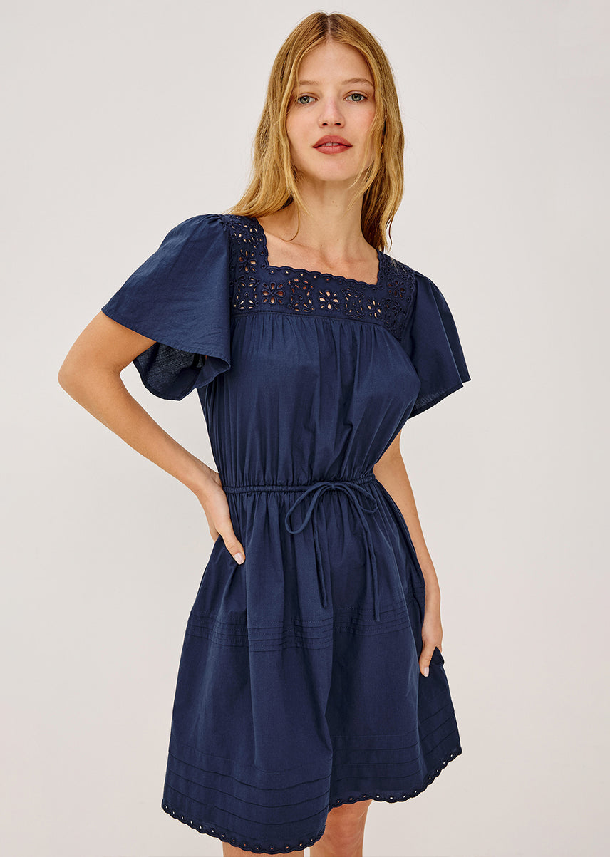 Woman wearing a navy blue dress with decorative neckline on a plain background