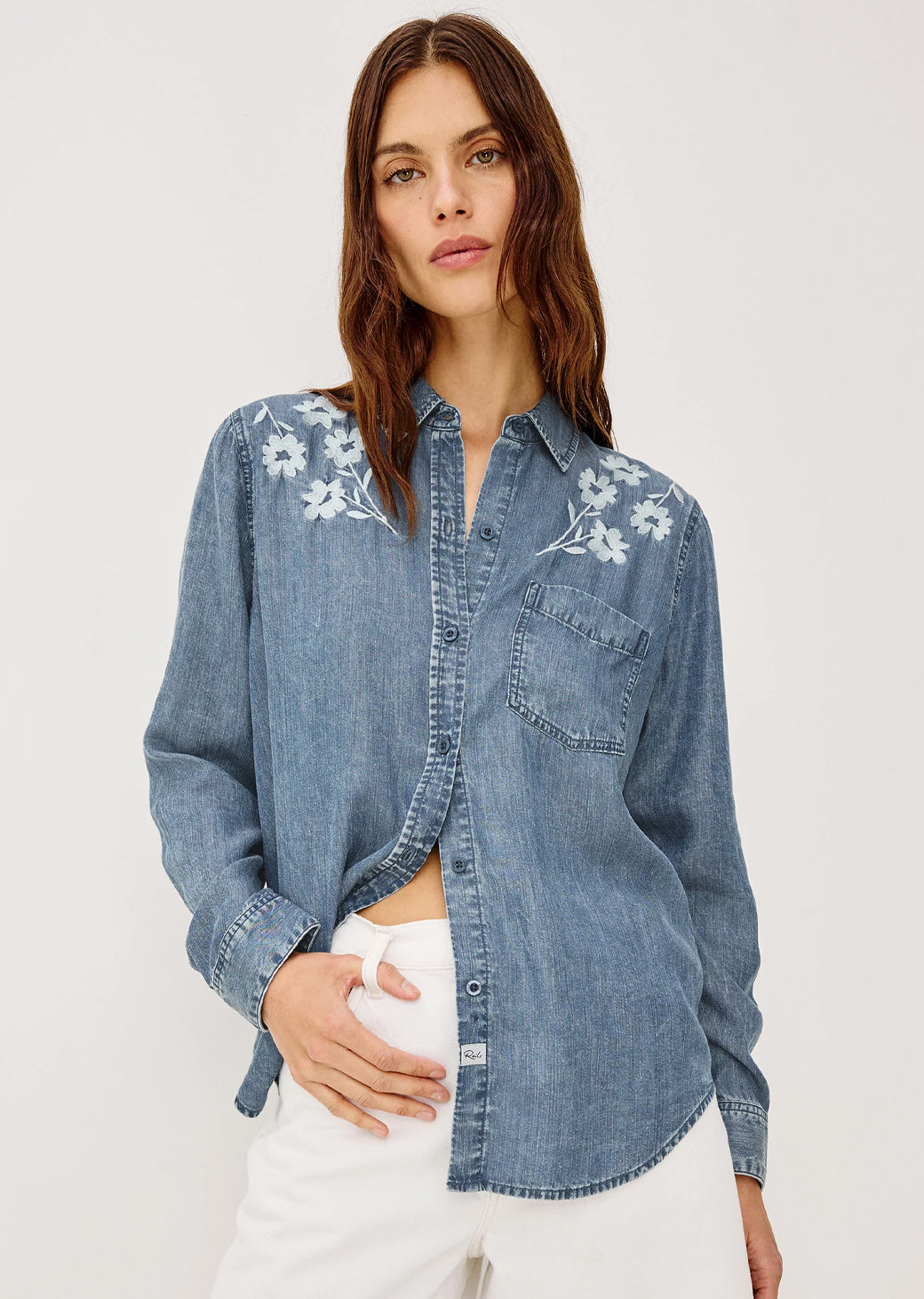 Woman wearing a denim shirt with floral embroidery on a plain background
