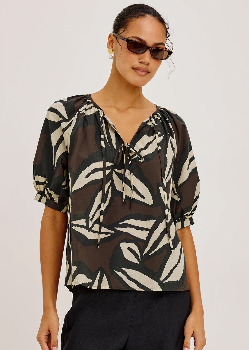 Woman wearing a black and white patterned blouse with puff sleeves on a plain background