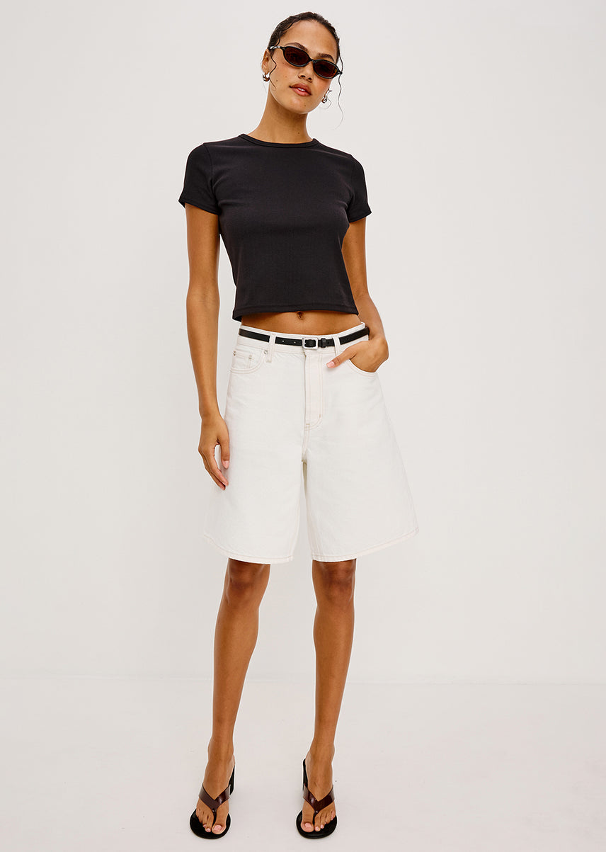 Woman in a black tee and long white shorts against an all white background
