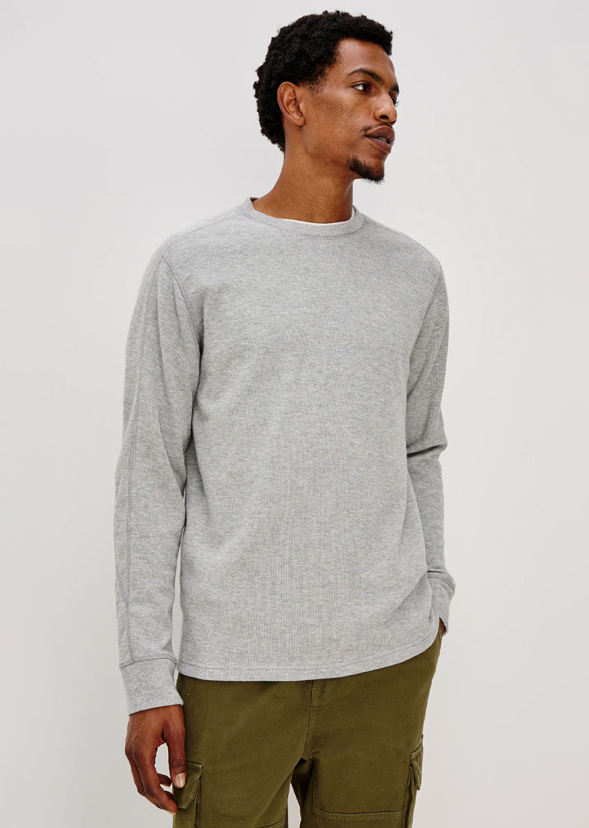 Man wearing a gray sweater and green pants against a white background