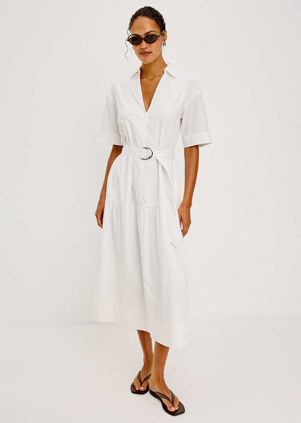 Woman wearing a white dress with a belt on a plain background