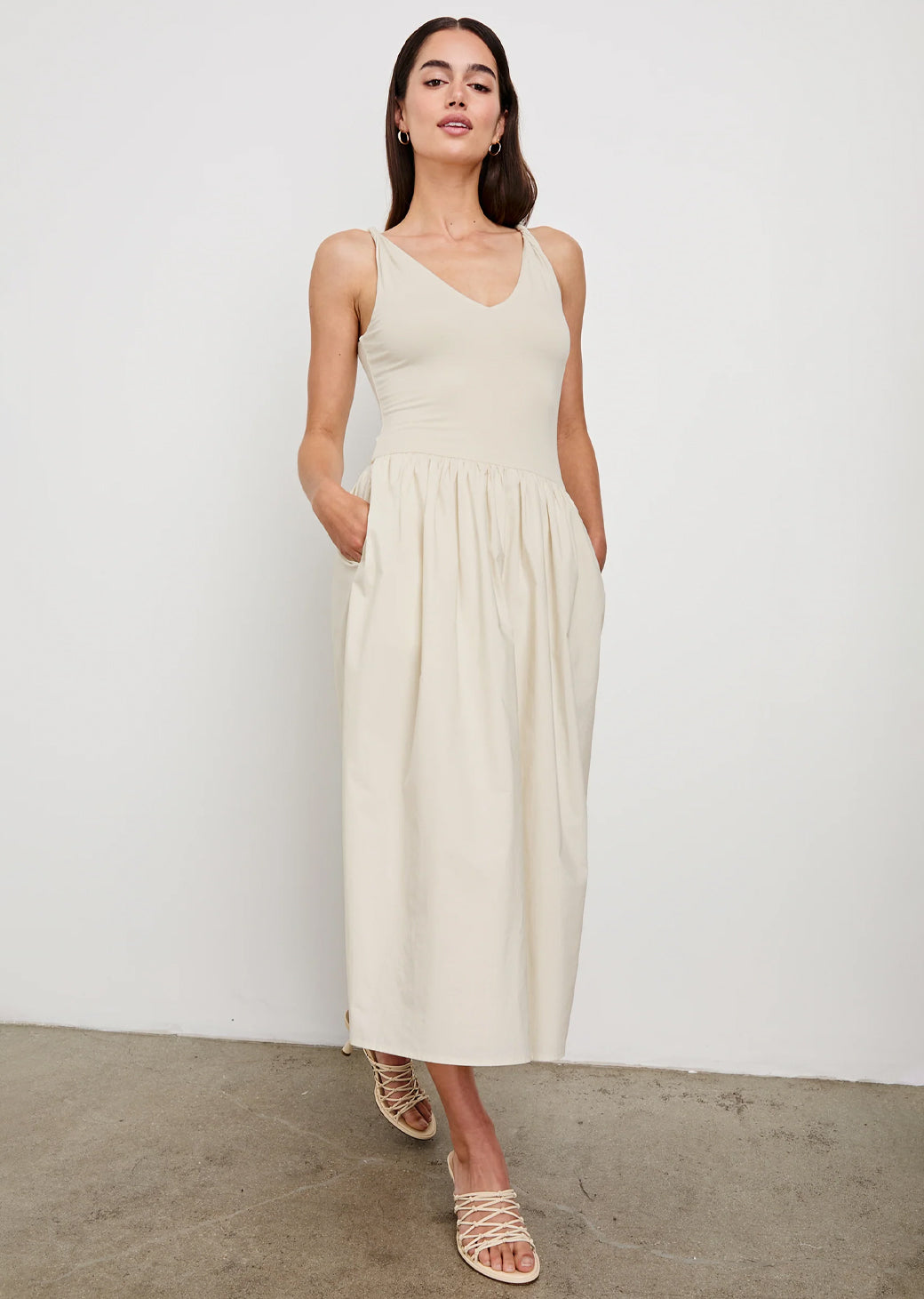 Woman wearing a beige sleeveless dress against a white background.