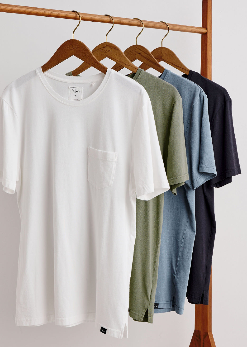 White t-shirt with green, blue, and black t-shirts on hangers against a white background