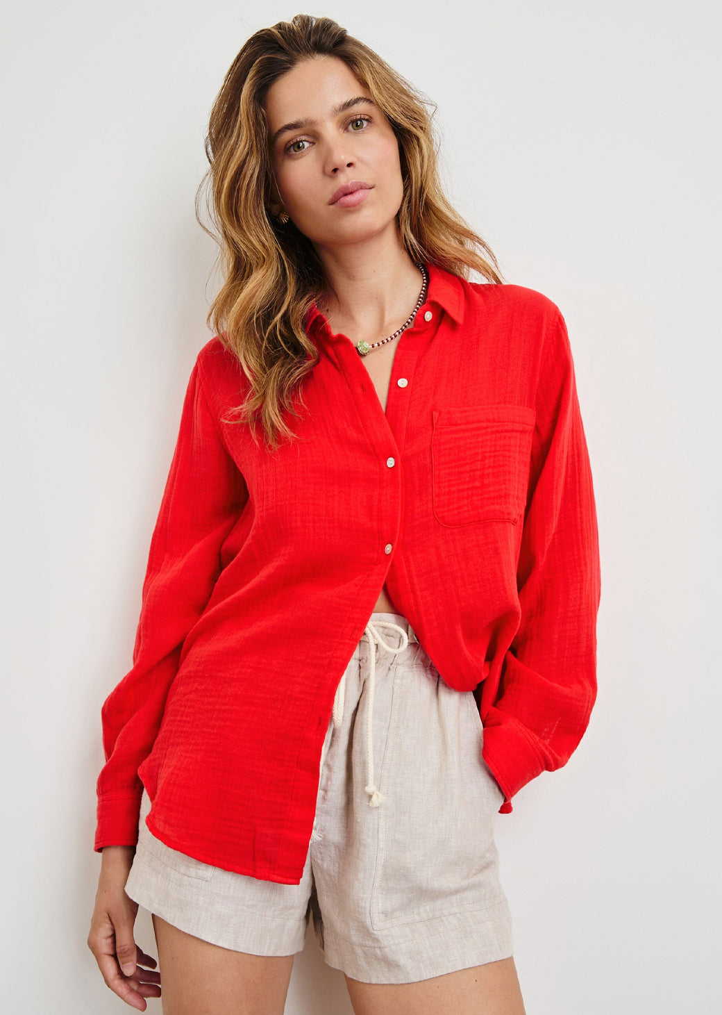 Woman wearing a red shirt and beige shorts against a white background