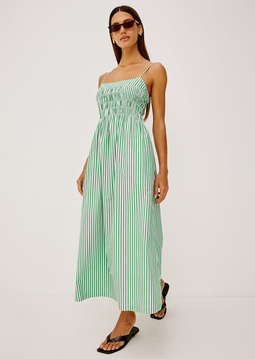 Woman in a green striped maxi dress dressed behind a white background
