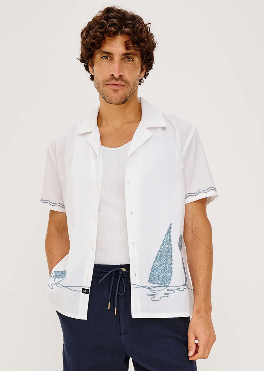 Man wearing a white shirt with a blue sail on it with dark blue pants
