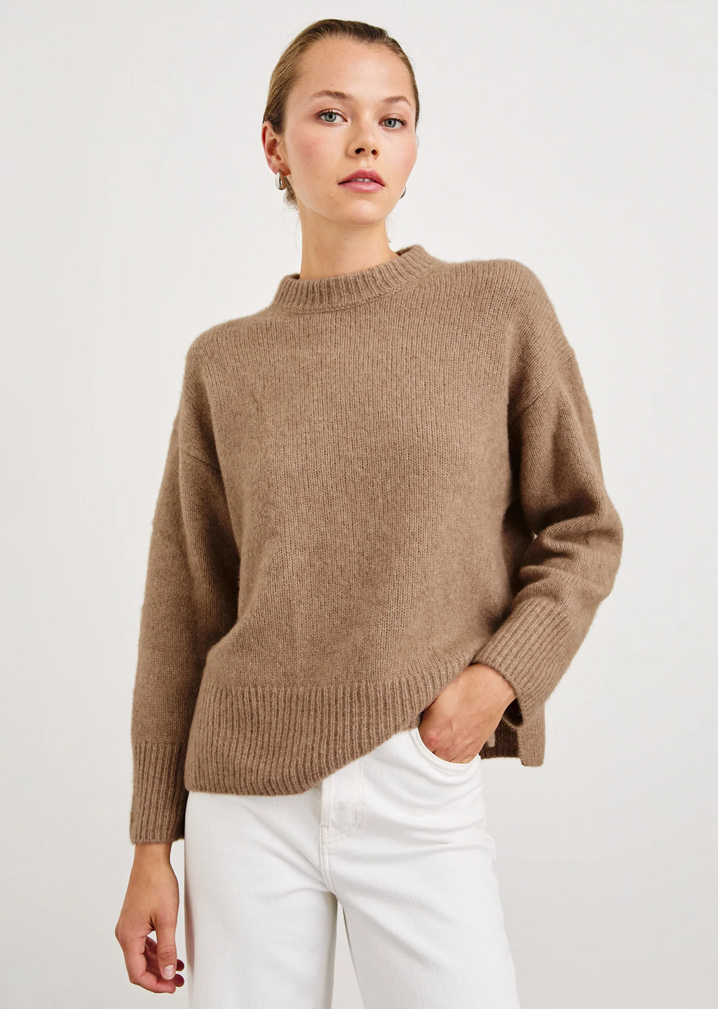 Woman wearing a brown sweater and white pants on a light background