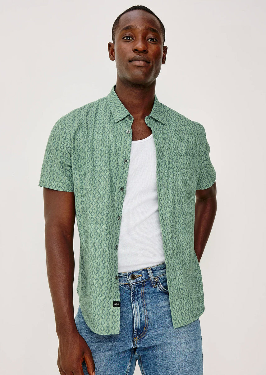Man wearing a green patterned shirt over a white t-shirt and blue jeans on a white background