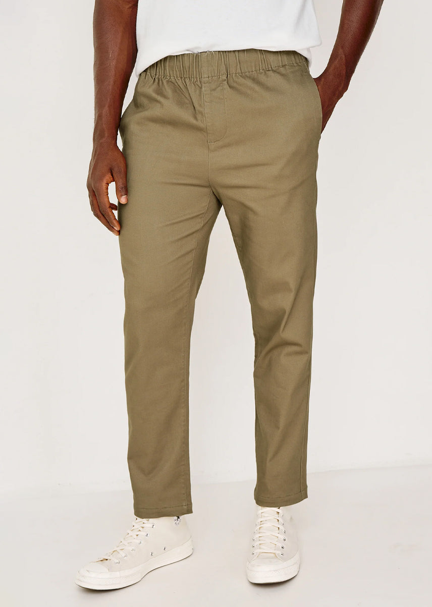 A person wearing slim-fit khaki trousers with an elastic waistband, paired with a white t-shirt and white sneakers, shown from the waist down against a plain light background.