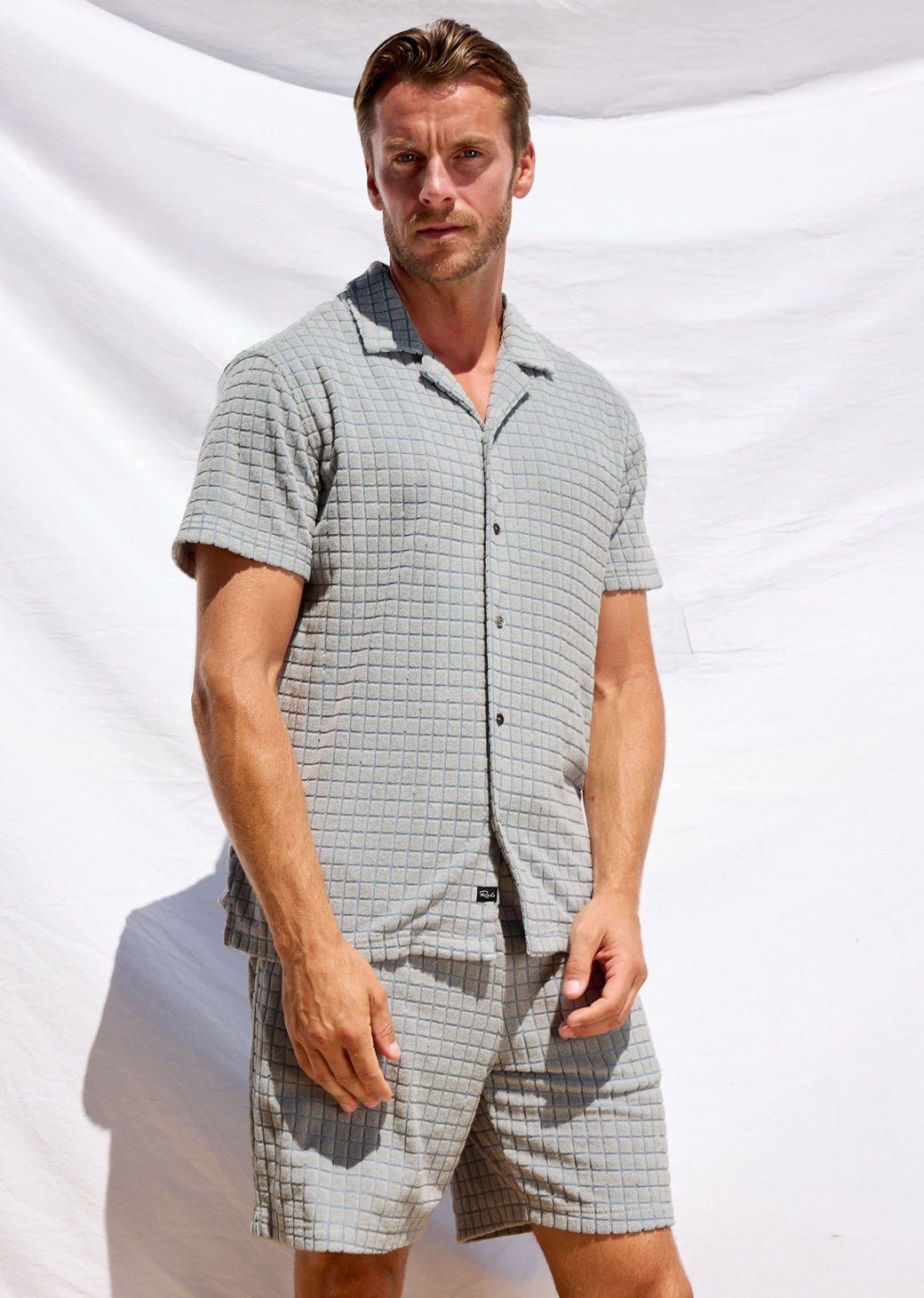 Man wearing a checkered shirt and shorts set against a white background