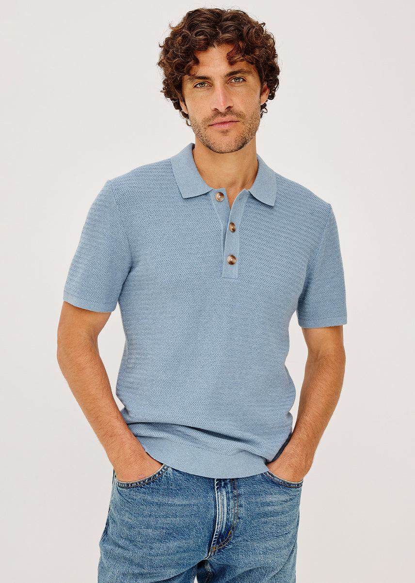 Man wearing a blue polo shirt and jeans on a light gray background
