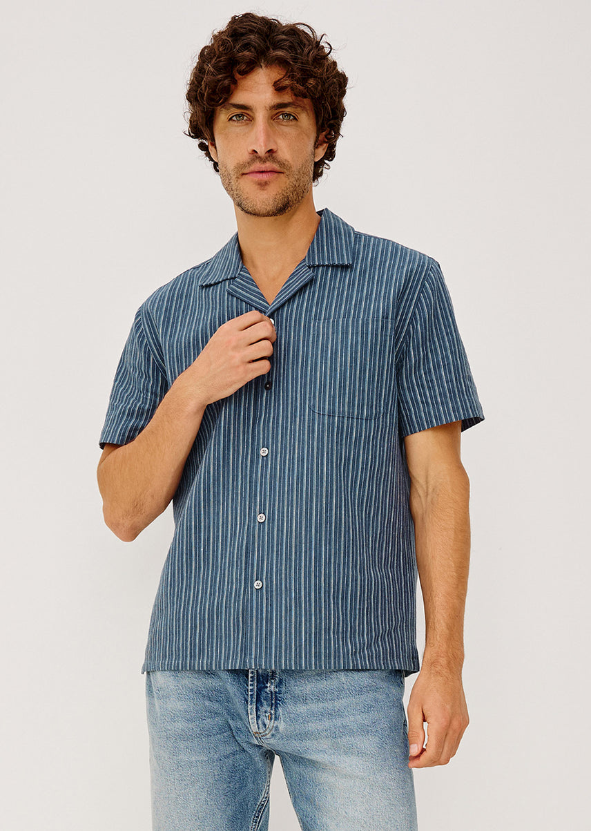 Man wearing a blue striped shirt and jeans on a light gray background