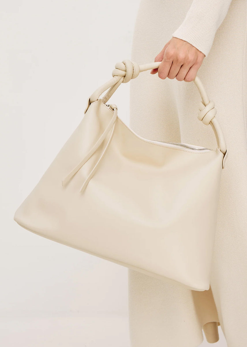 Beige handbag held by a person wearing a white outfit on a light gray background