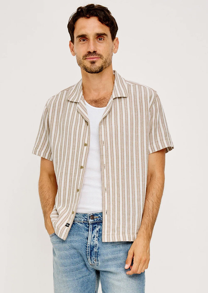 Man wearing a striped shirt over a white t-shirt and jeans on a plain background