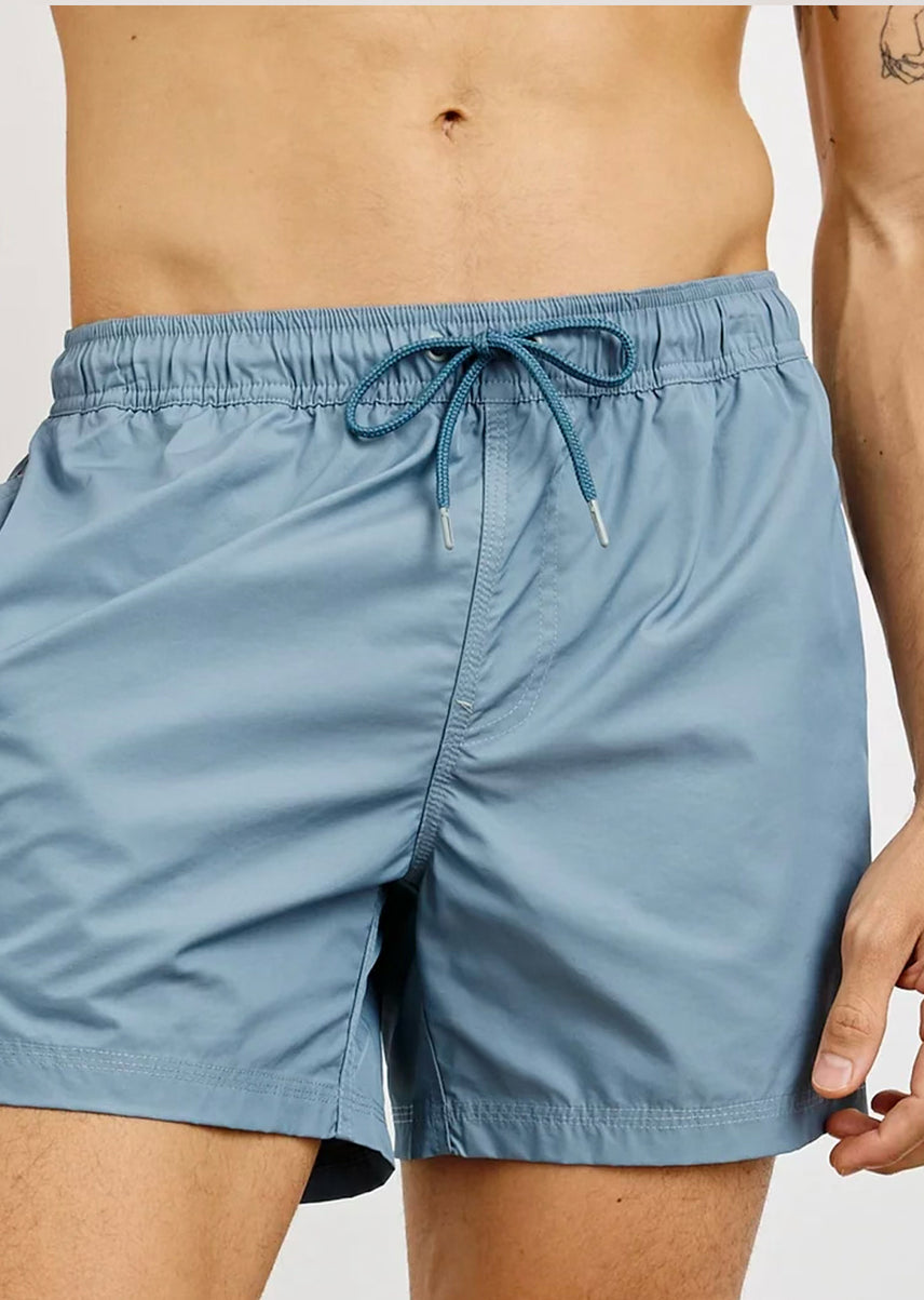Blue swim shorts worn by a person on a plain background