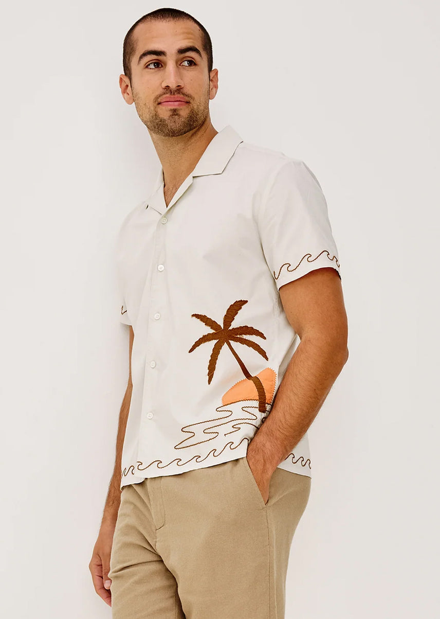 Man wearing a white shirt with a palm tree design on a plain background