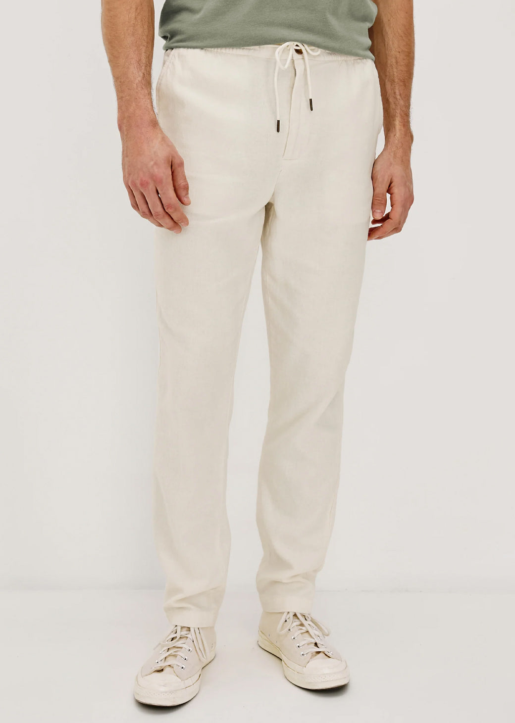 Man wearing white pants and a green shirt on a plain background