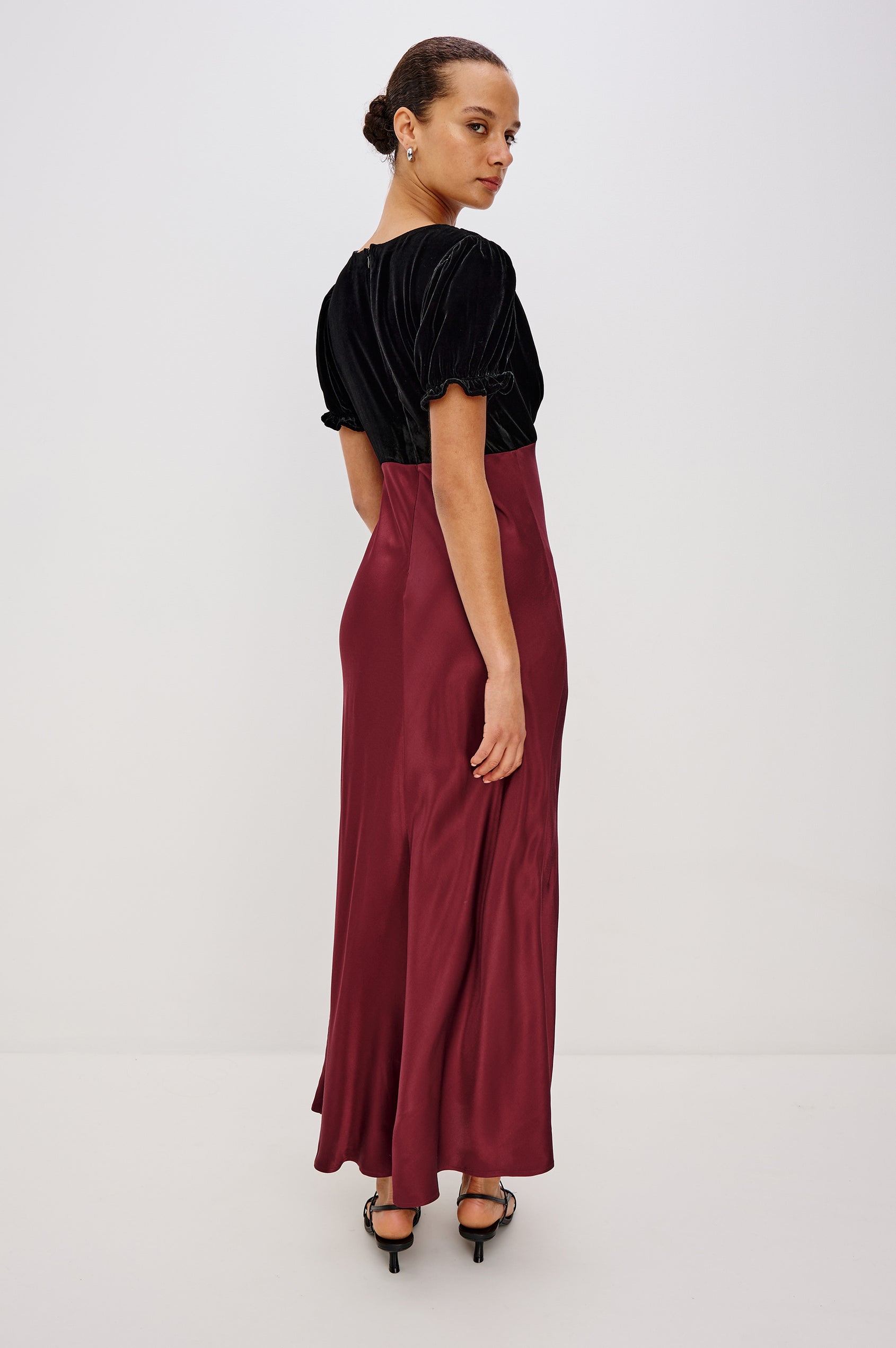 A garnet velvet maxi dress with a fitted V-neck bodice and adjustable center-bust ties. The bias-cut skirt drapes elegantly to ankle length, finished with a back zipper closure. Back View on Model.